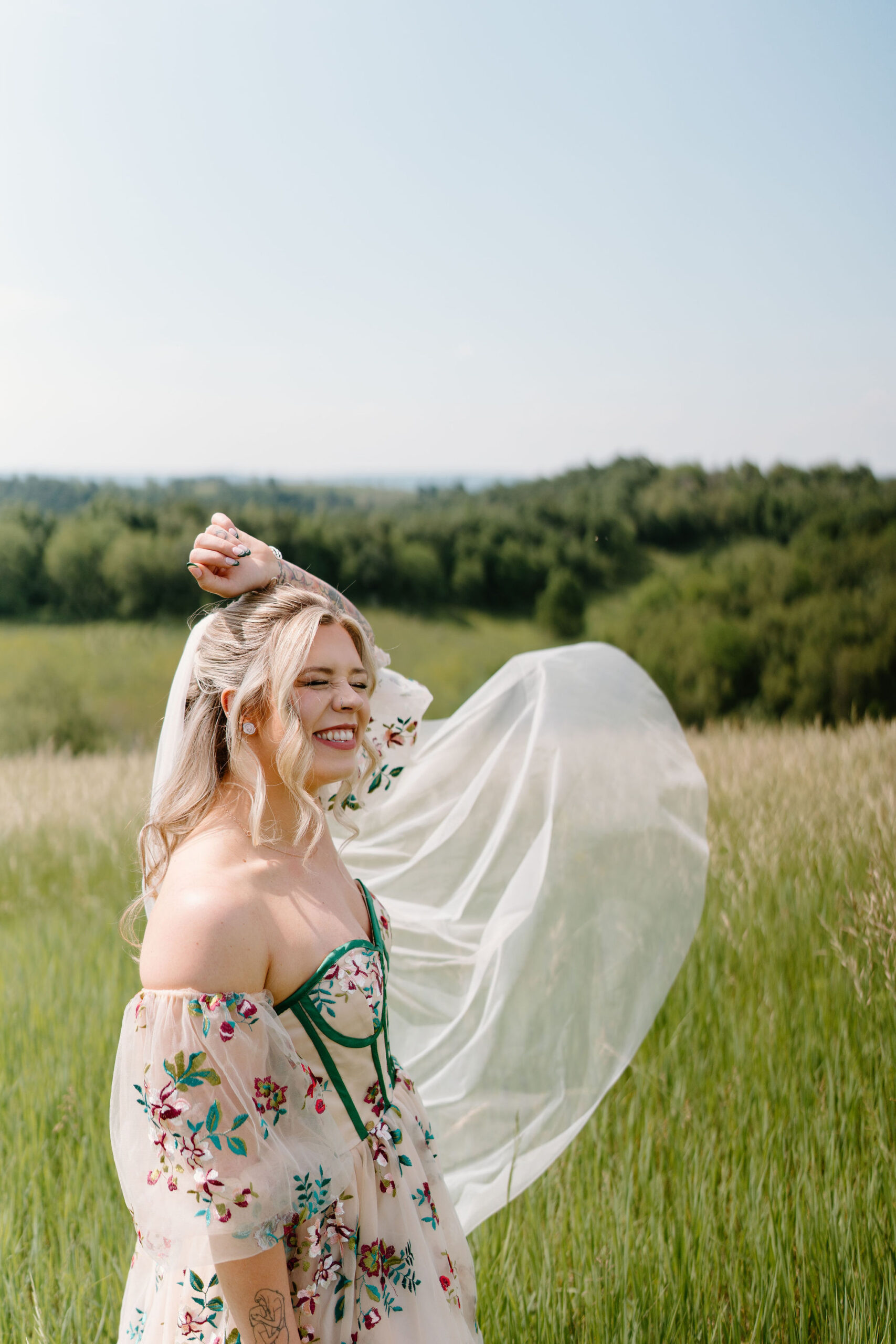 bride smiling widely with one hand thrown over her head, her veil flowing in the wind