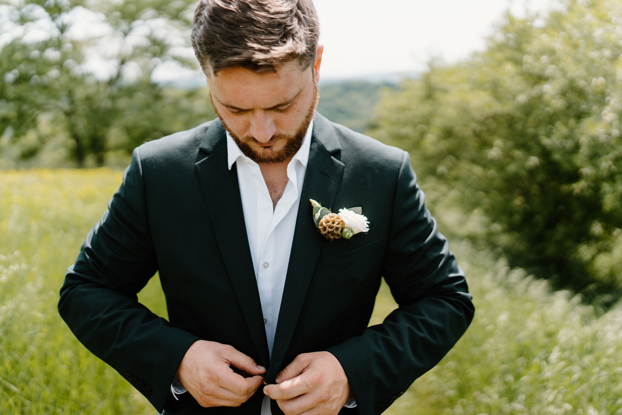 close up image of the groom (green suit) buttoning his suit jacket