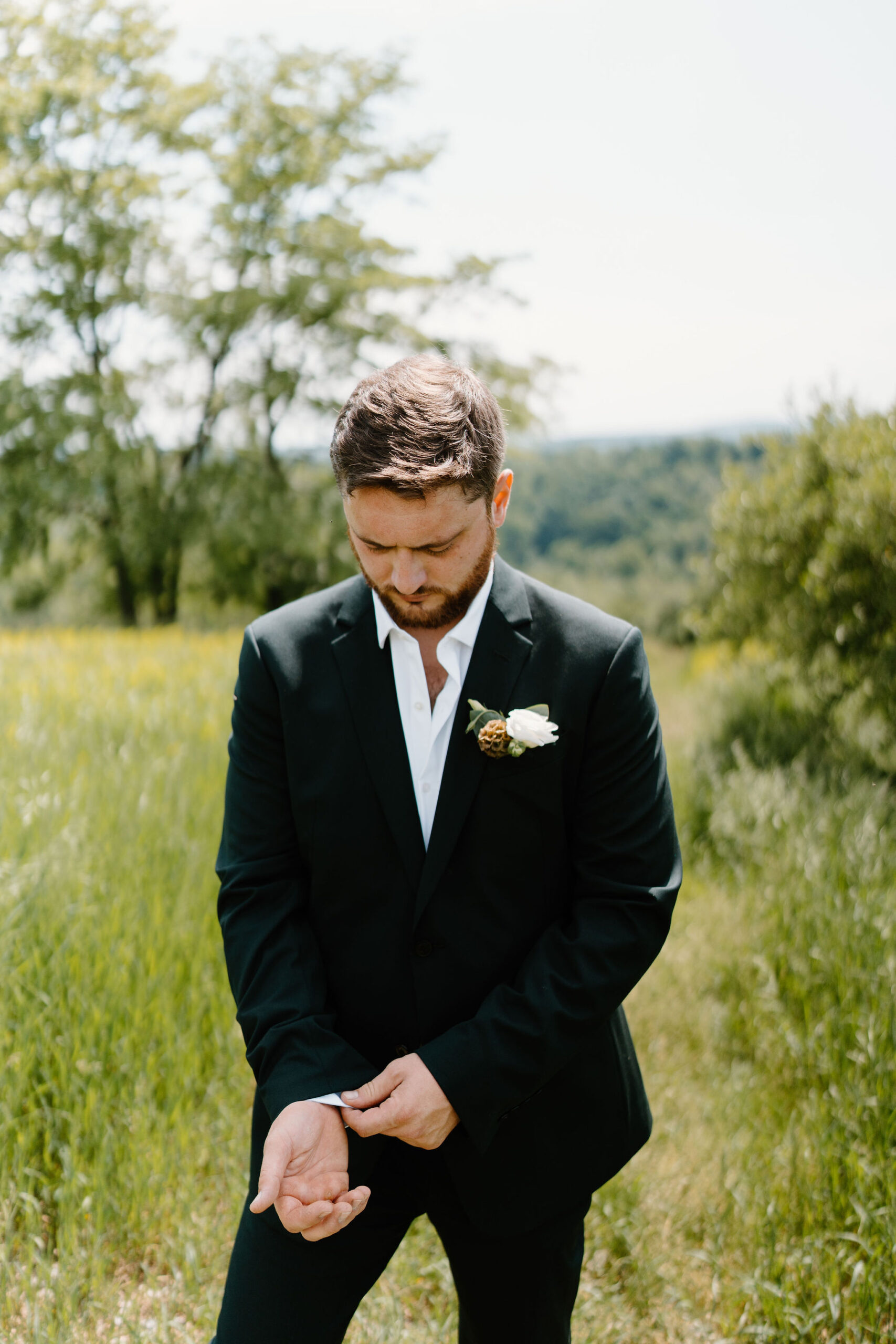 groom in a dark green suit with a boutonniere fixing his cuff links