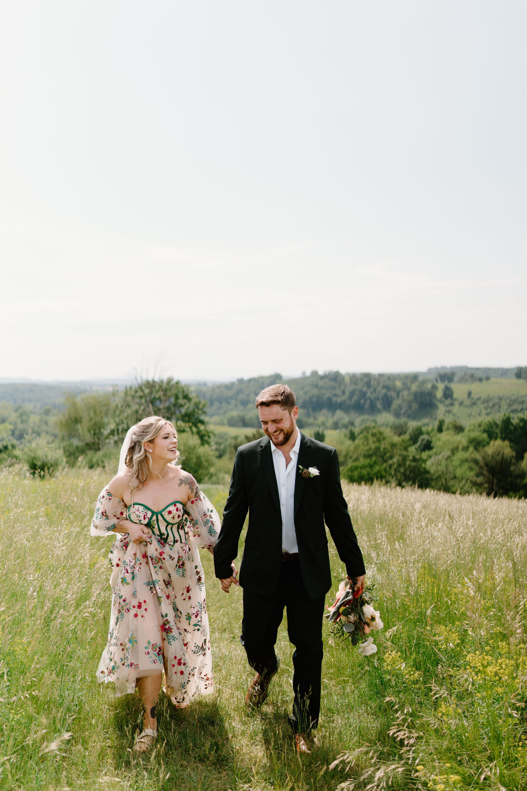 bride and groom holding hands and laughing with each other as they walk through an overgrown grassy field in Lehigh Valley, Pennsylvania