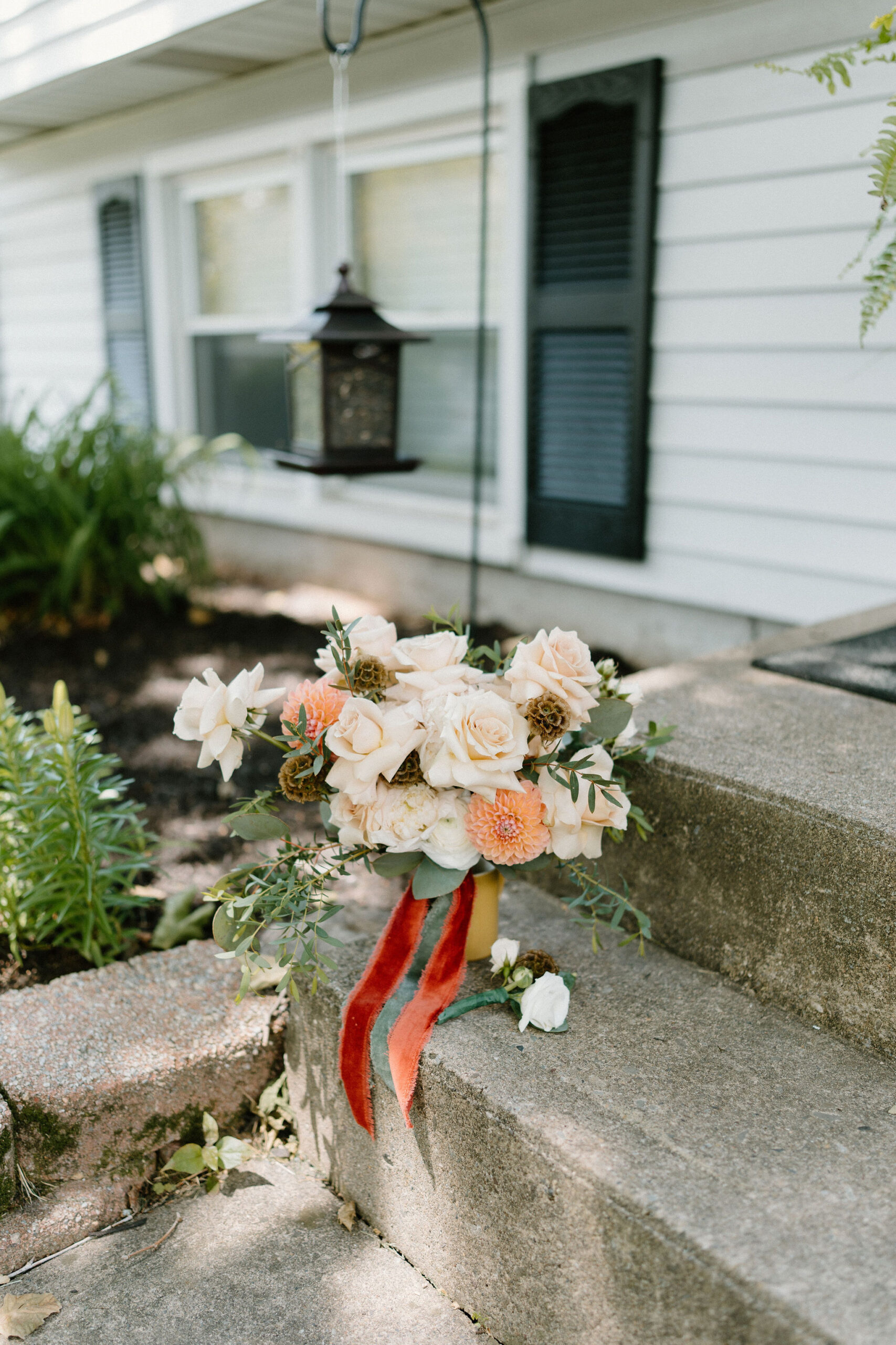 wedding detail image of a bridal bouquet of pink roses and greenery outside on a front step to a home, with a boutonniere next to it.
