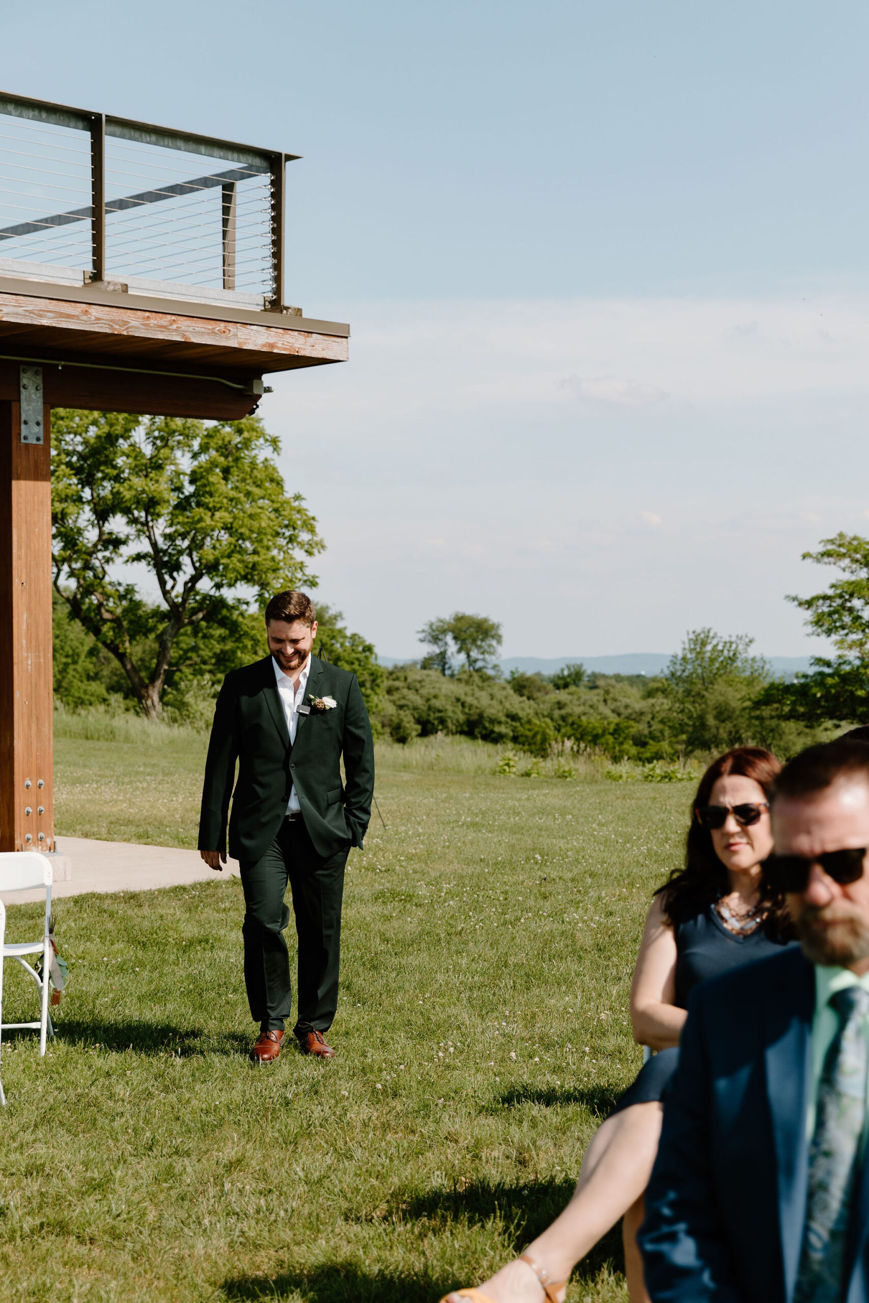 groom in a dark green suit smiling as he walks down the aisle to his wedding ceremony