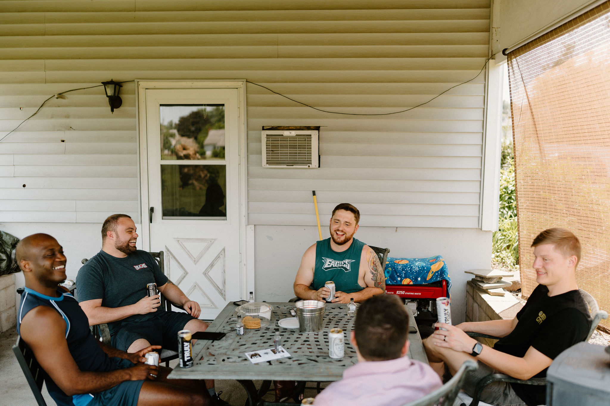 groom and his groomsmen sitting outside on a covered patio around a table, drinking and smiling while they talk