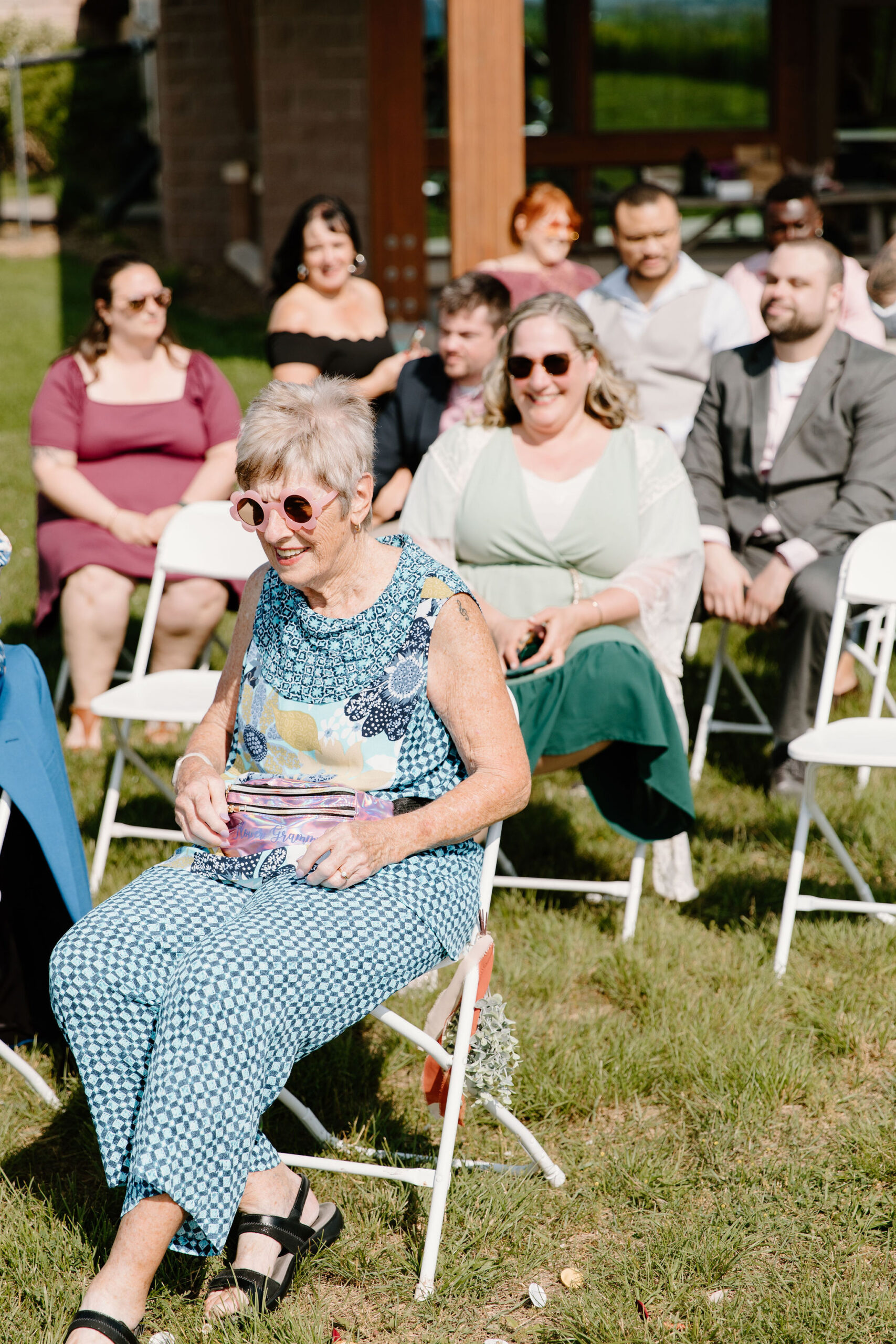 grandmother of the bride in a colorful blue outfit and fun sunglasses, sitting for the ceremony