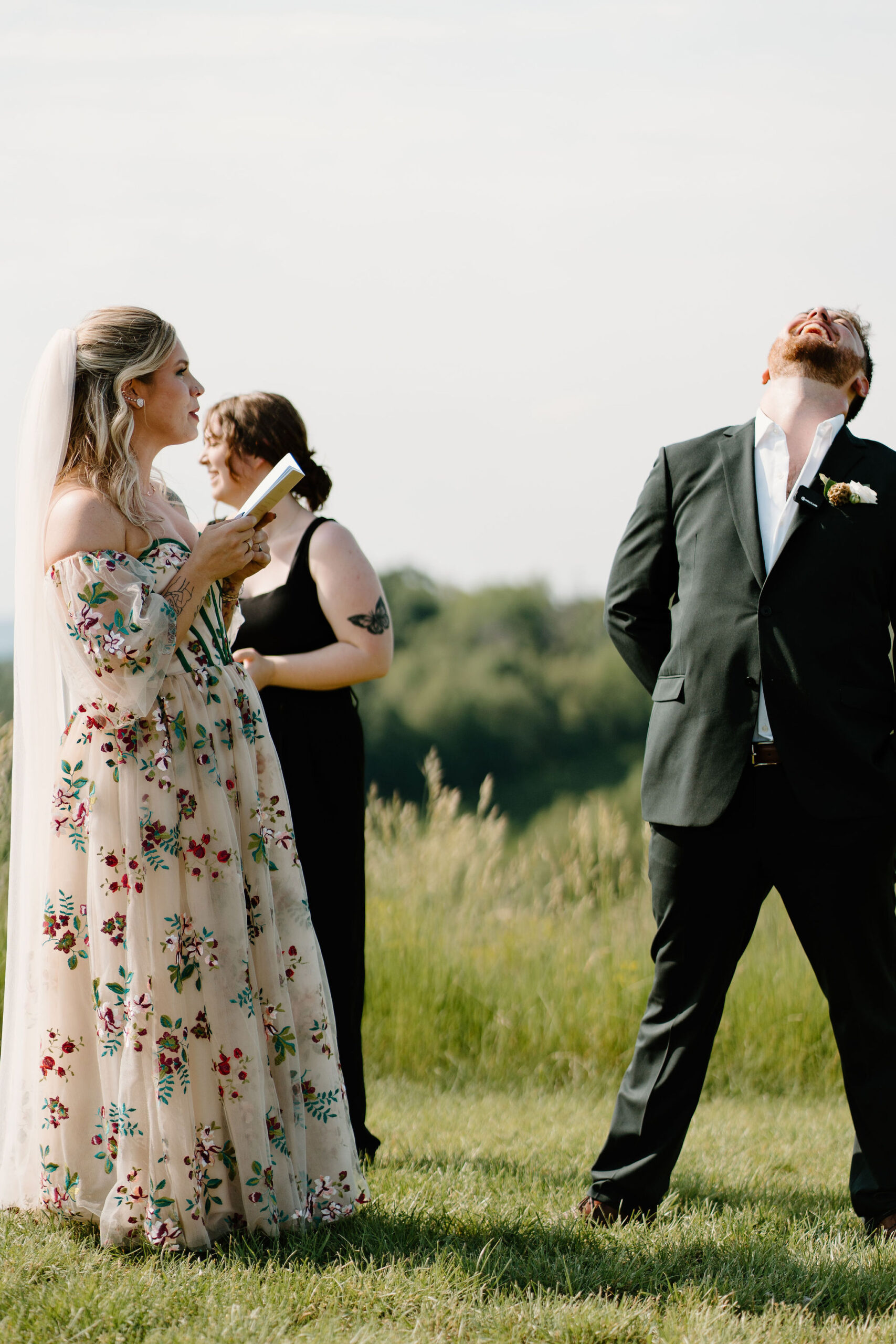 groom laughing with his head thrown back during his wedding ceremony, while bride reads her vows to him.