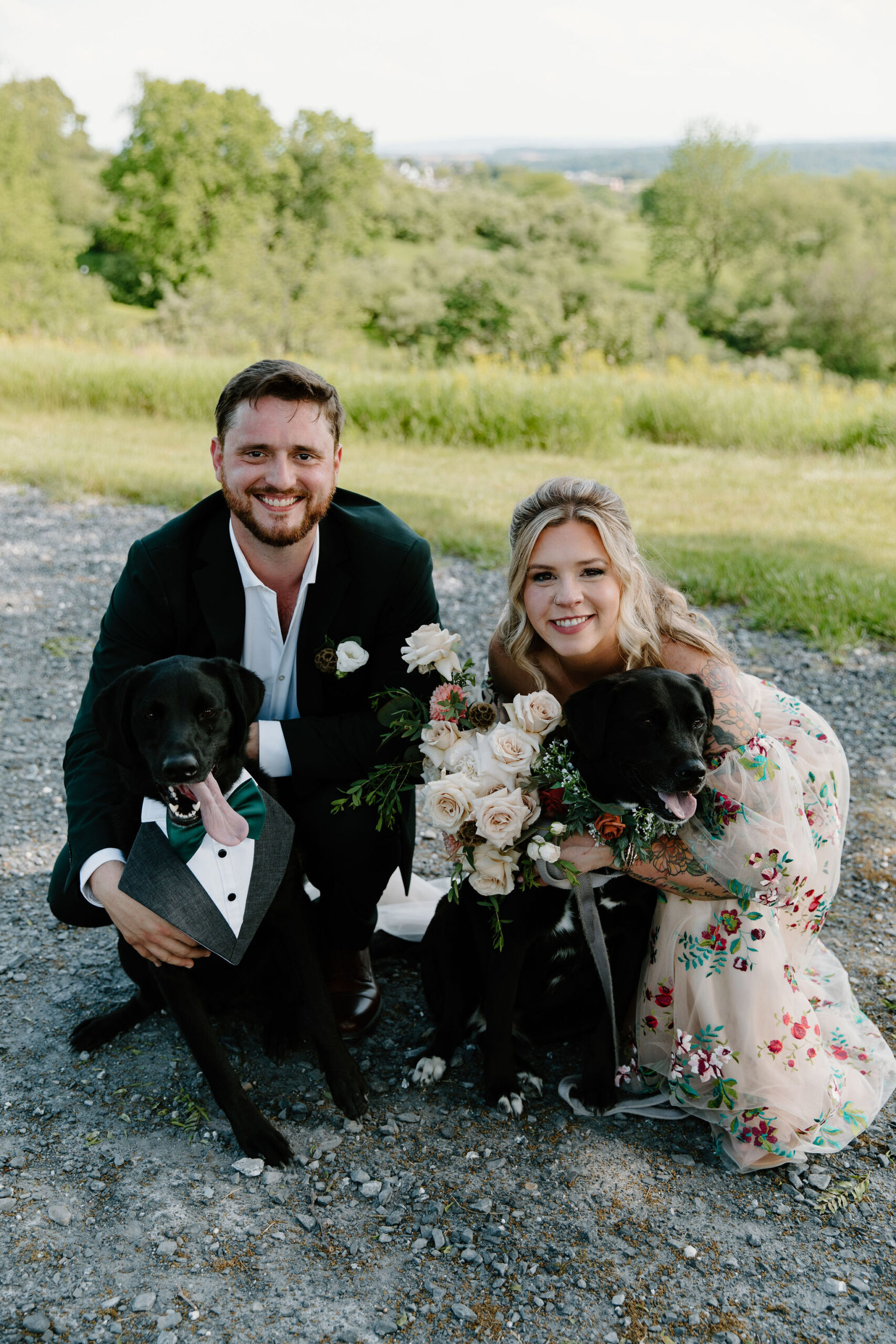 bride and groom kneeling down and smiling at the camera for a photo with their two black labs
