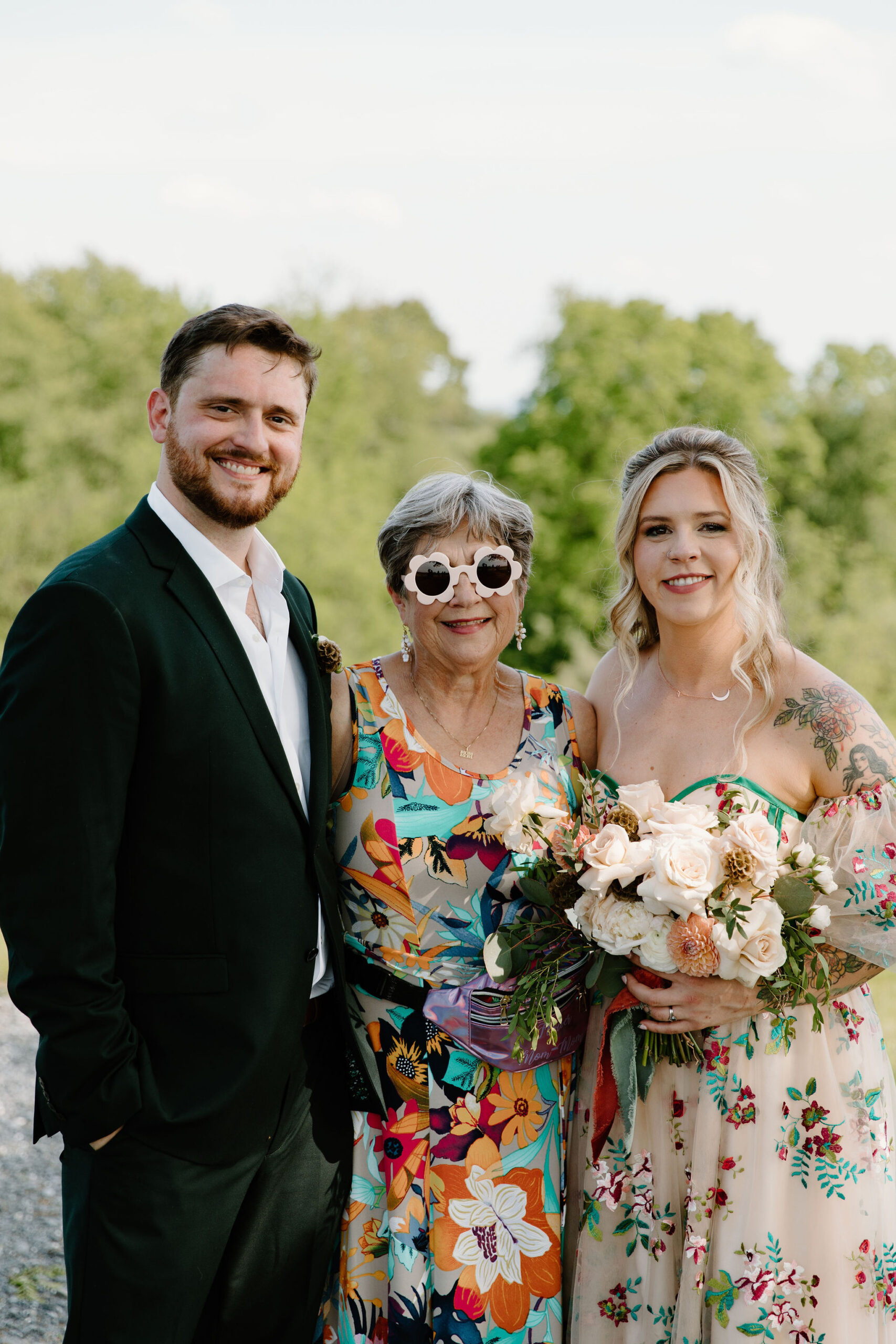 bride and groom smiling with a grandmother, wearing a colorful dress and flower sunglasses