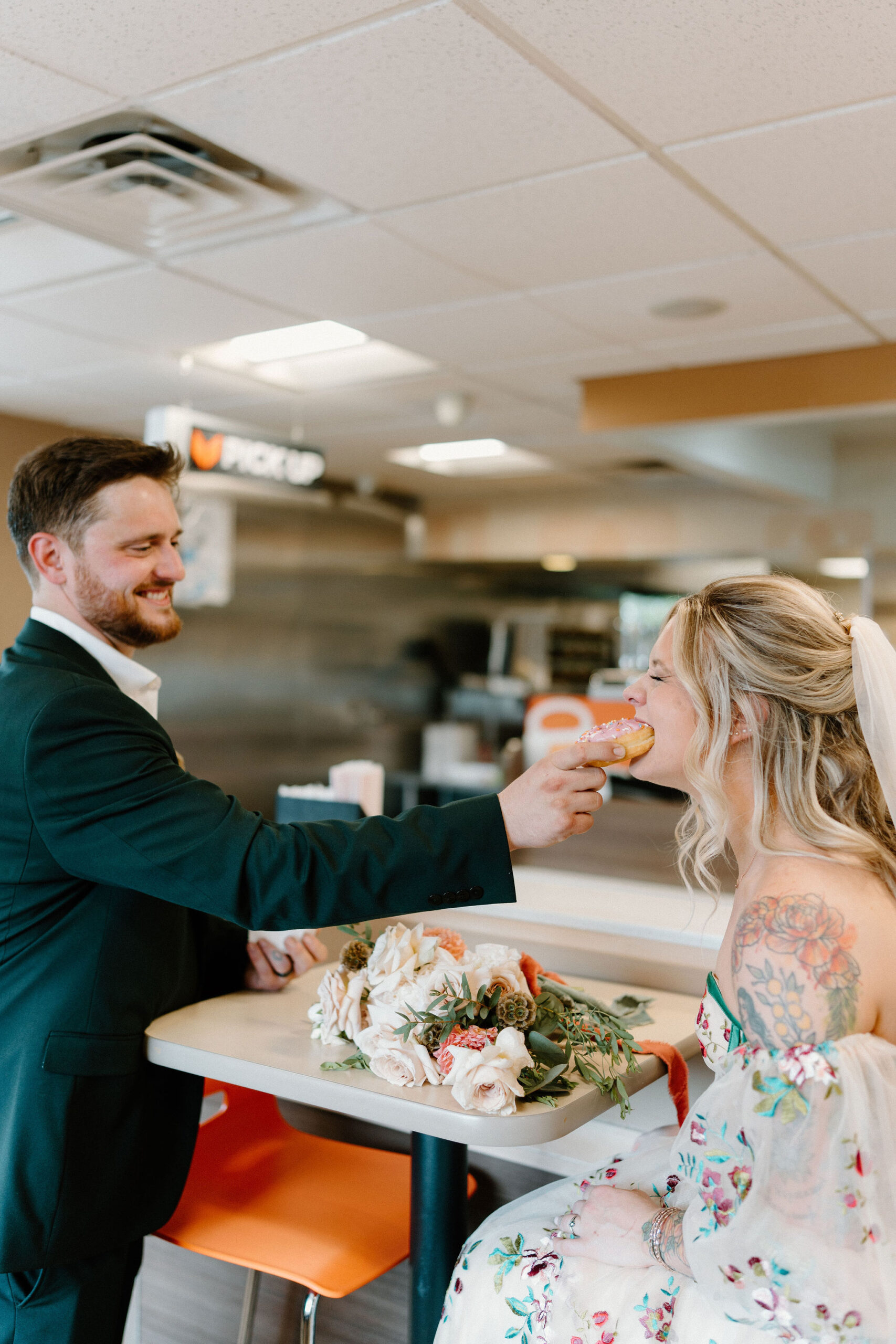 groom feeding his bride a bite of a donut inside a Dunkin Donuts