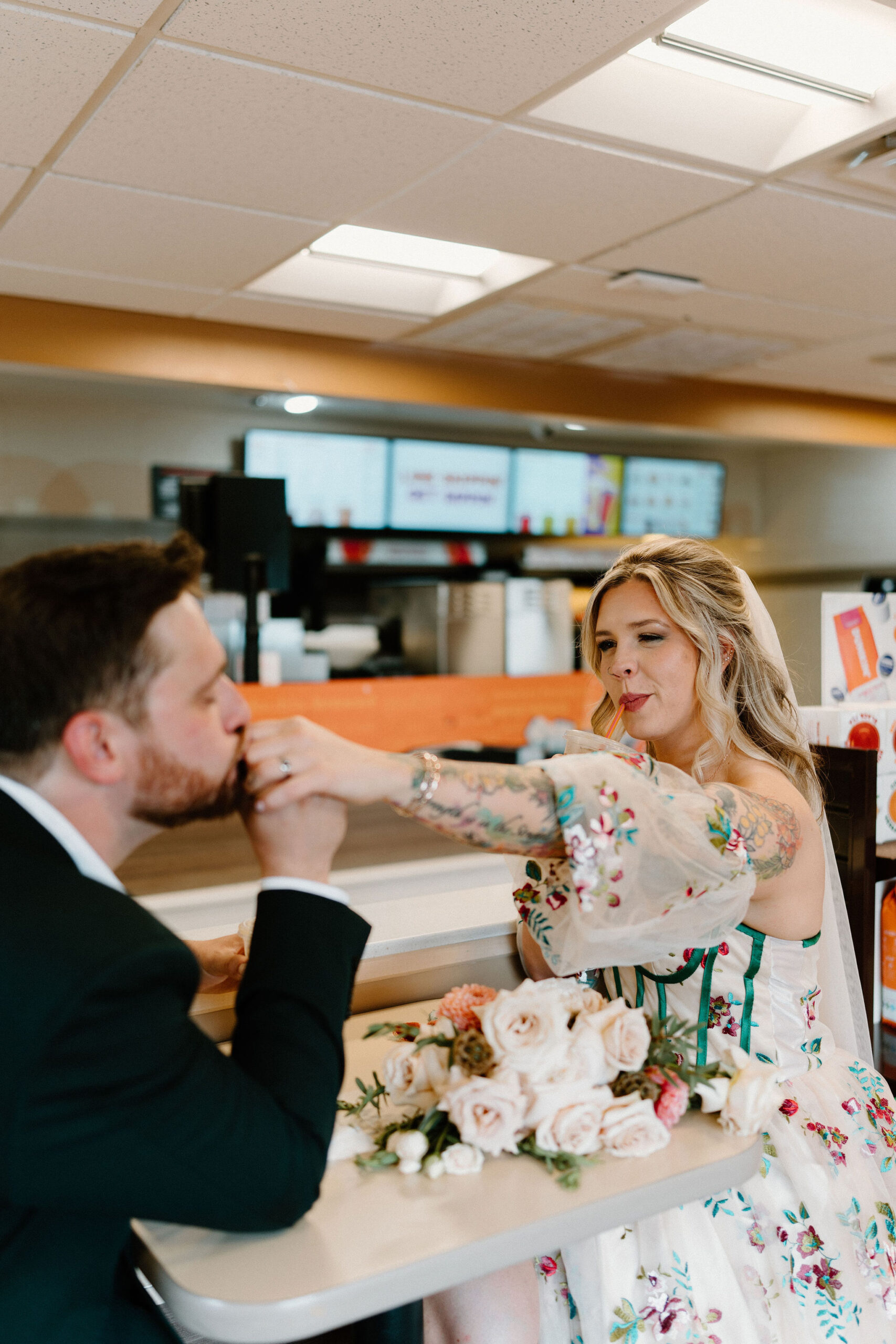 groom kissing bride's hand while she sits across the table, smiling and having a sip of her coffee