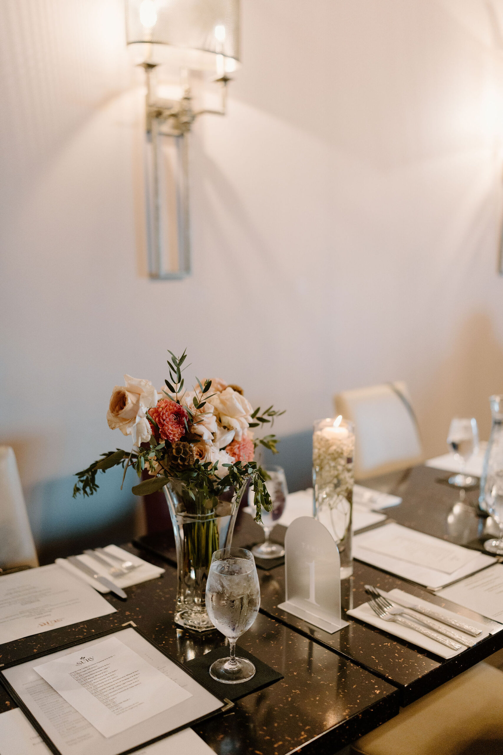 centerpiece for a wedding reception indicating "table 1" with a bouquet of white and pink flowers and greenery
