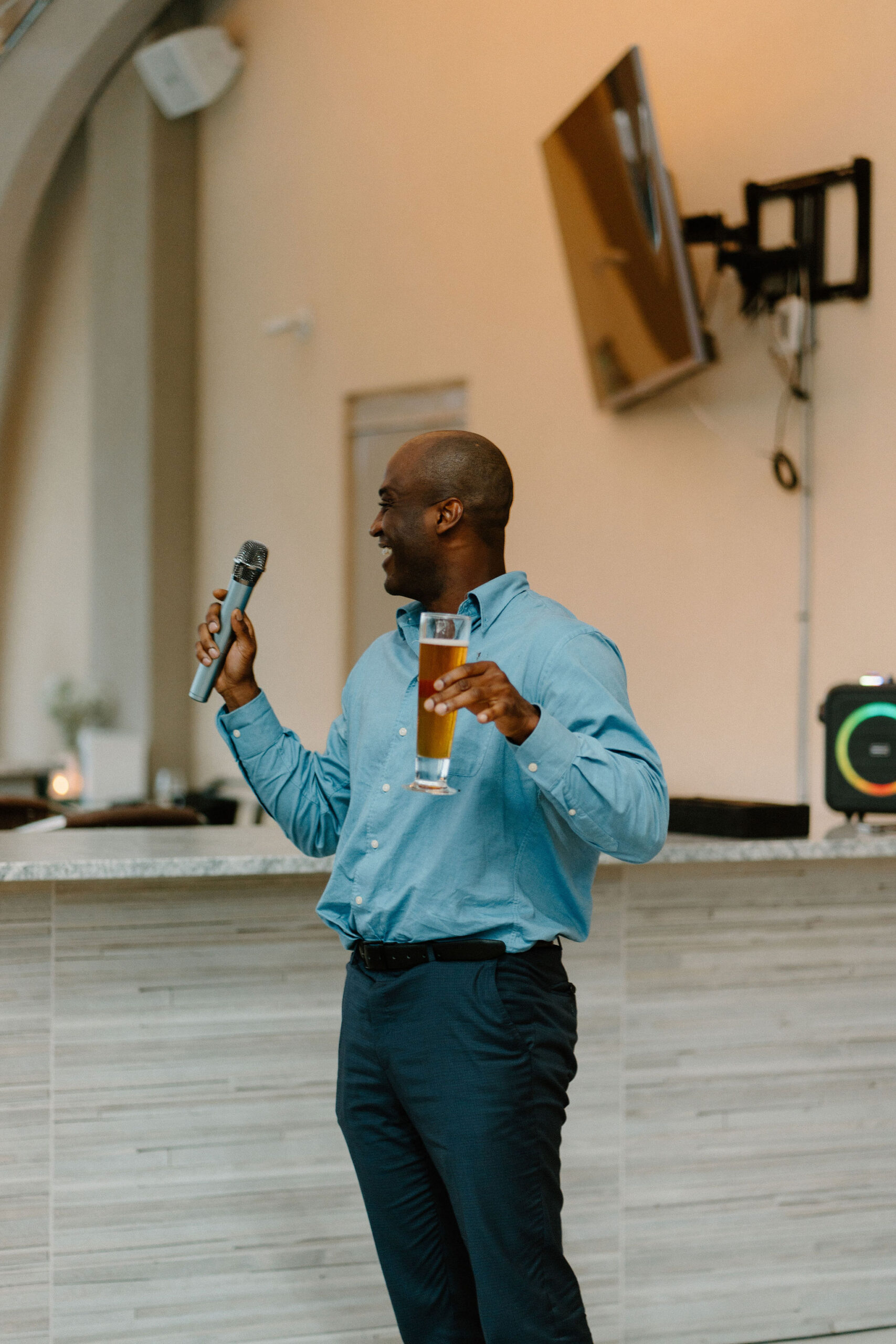 groom's best friend smiling as he holds up a beer and a microphone for his speech