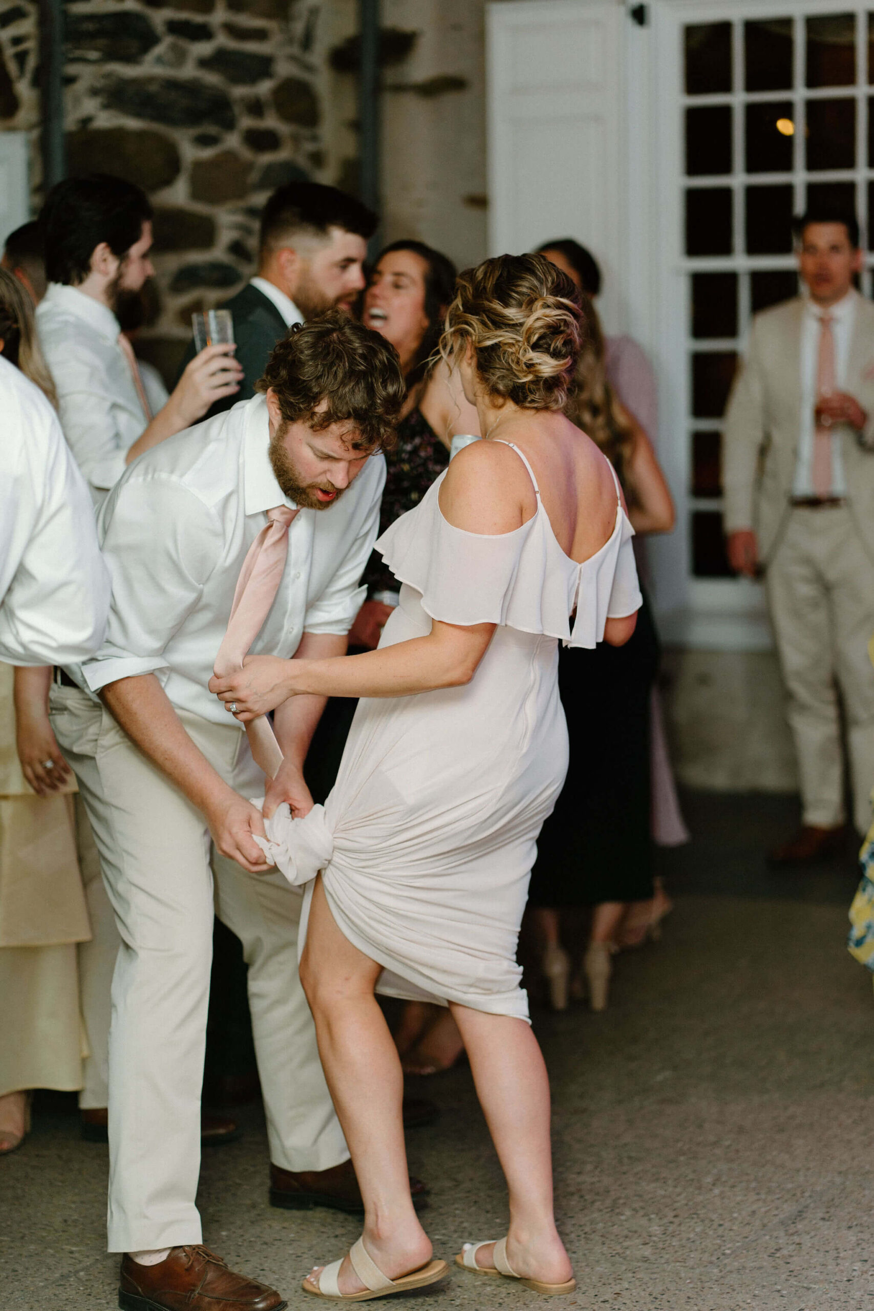 bridesmaid's husband tying up the skirt of her dress so she can dance during wedding reception