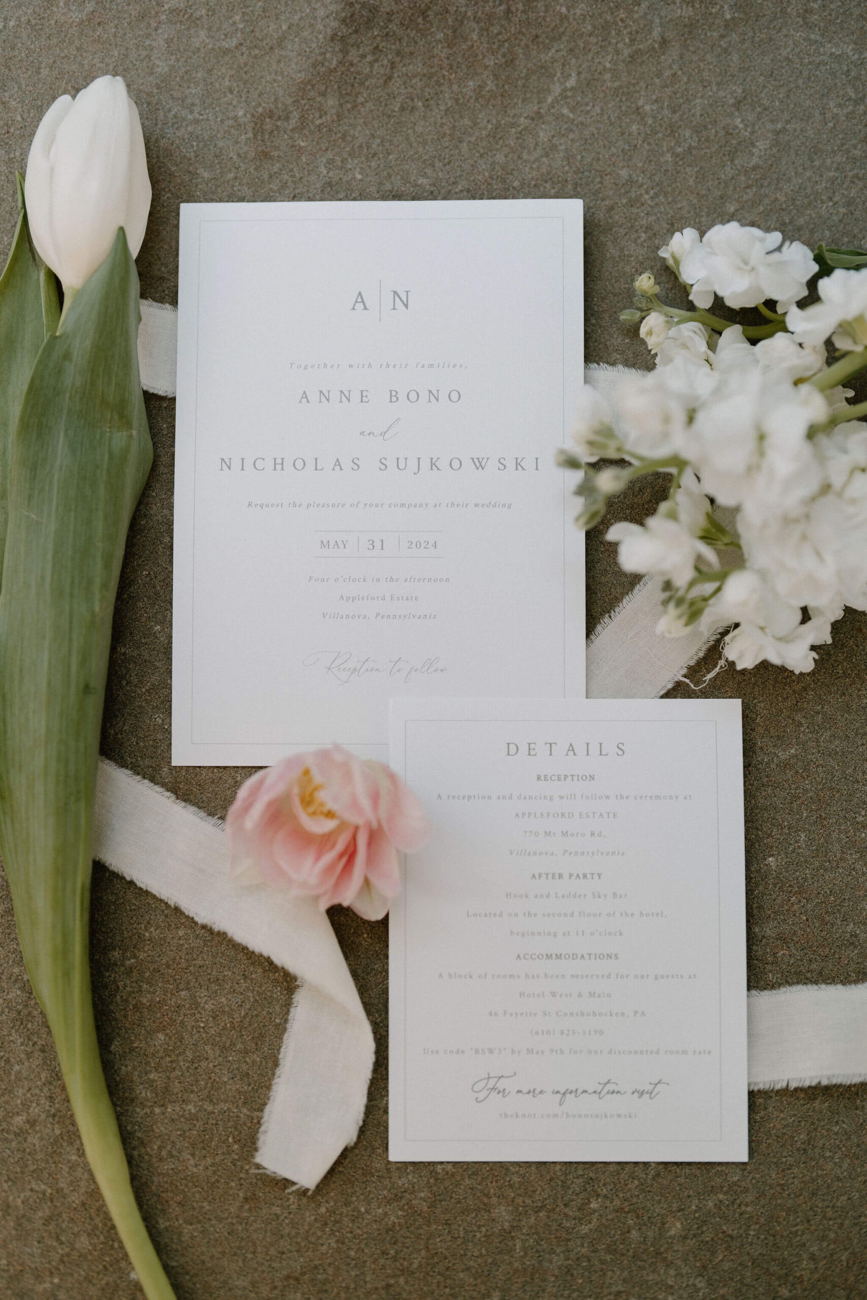 Details photos of a minimalistic wedding invitation suite, surrounded by a white tulip, dainty white flowers, and a pink tulip, with a white ribbon zigzagging behind it