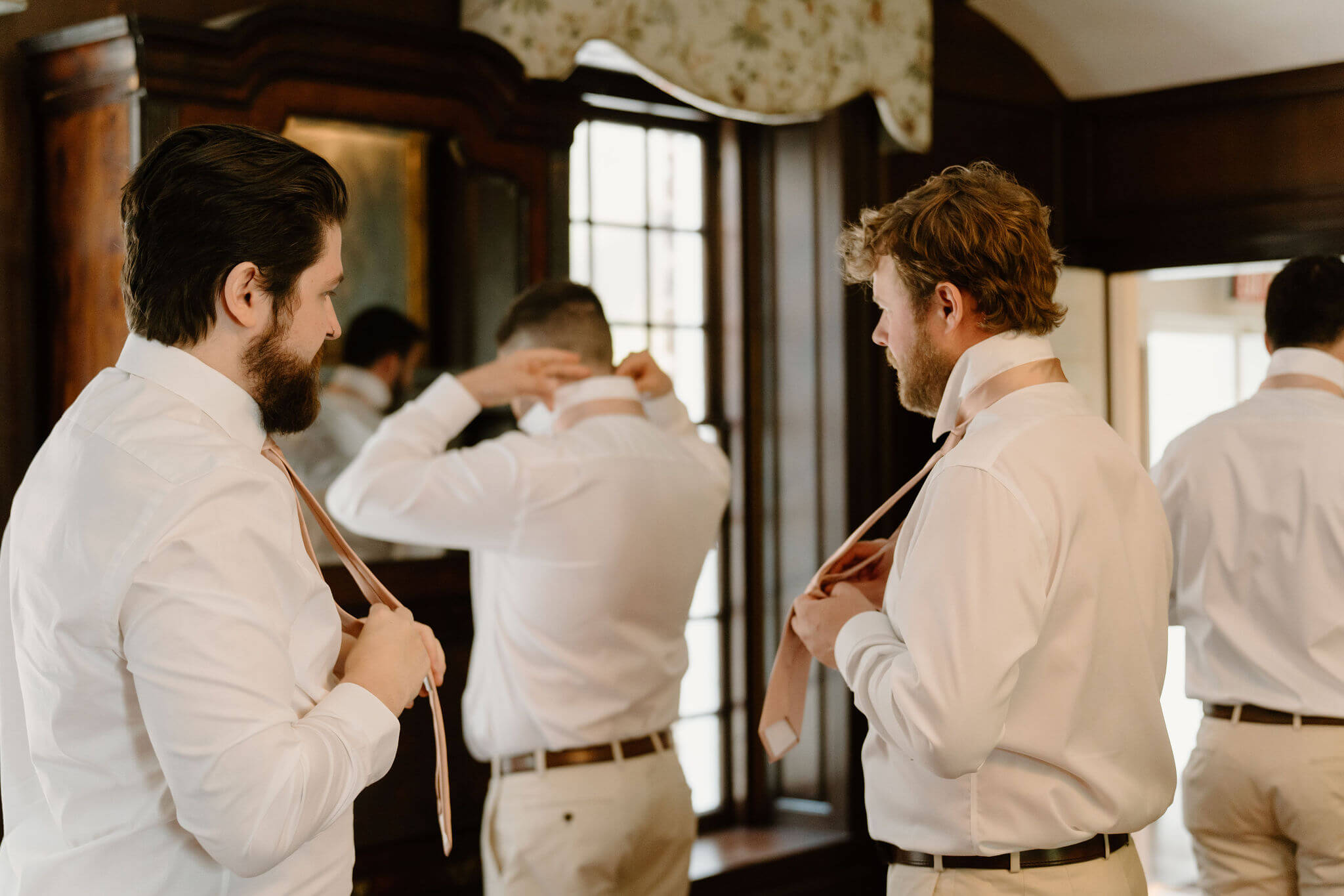 groom and groomsmen in a dark wooden room, getting dressed and fixing their ties