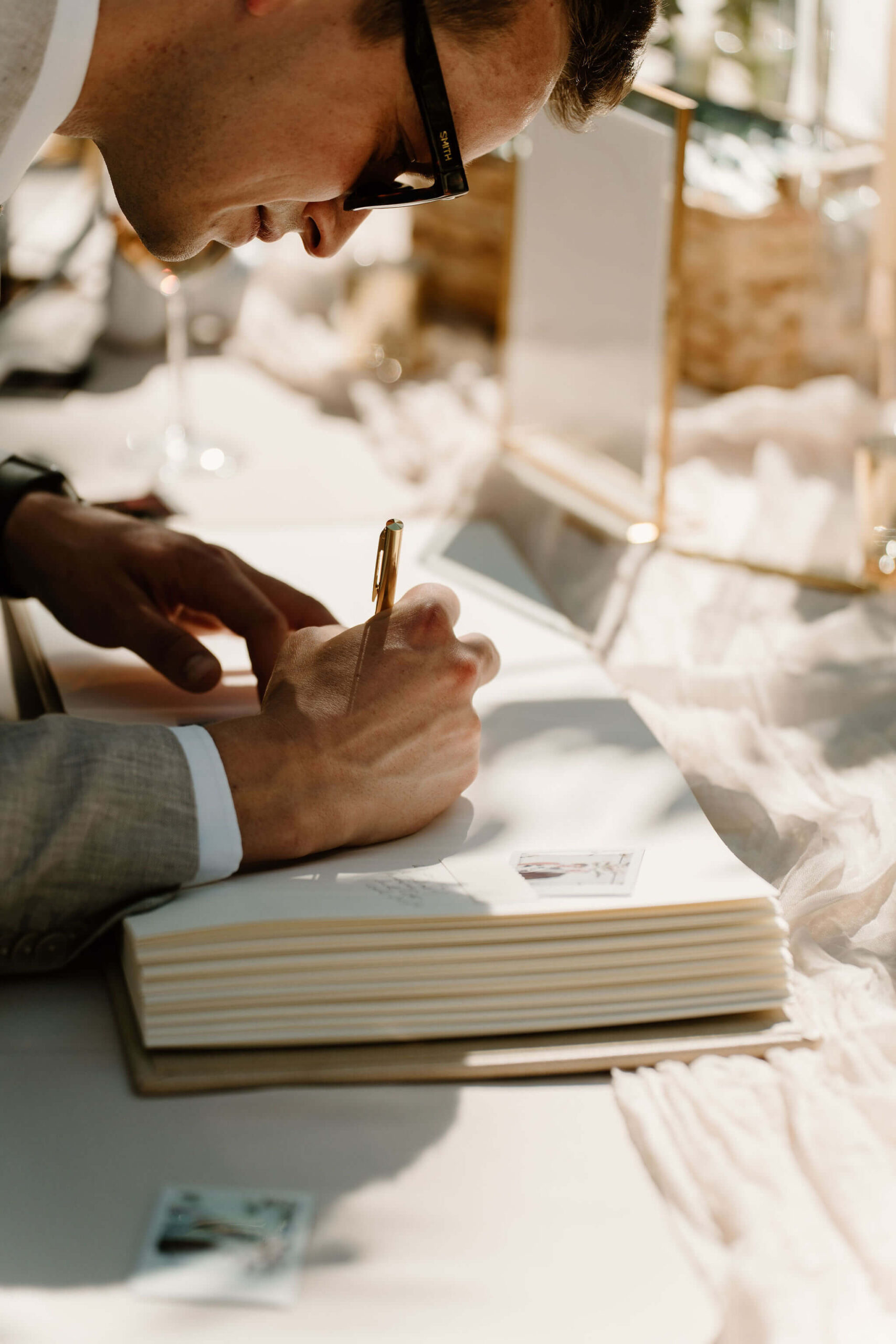 guest wearing sunglasses and gray suit leaning over to sign guest book