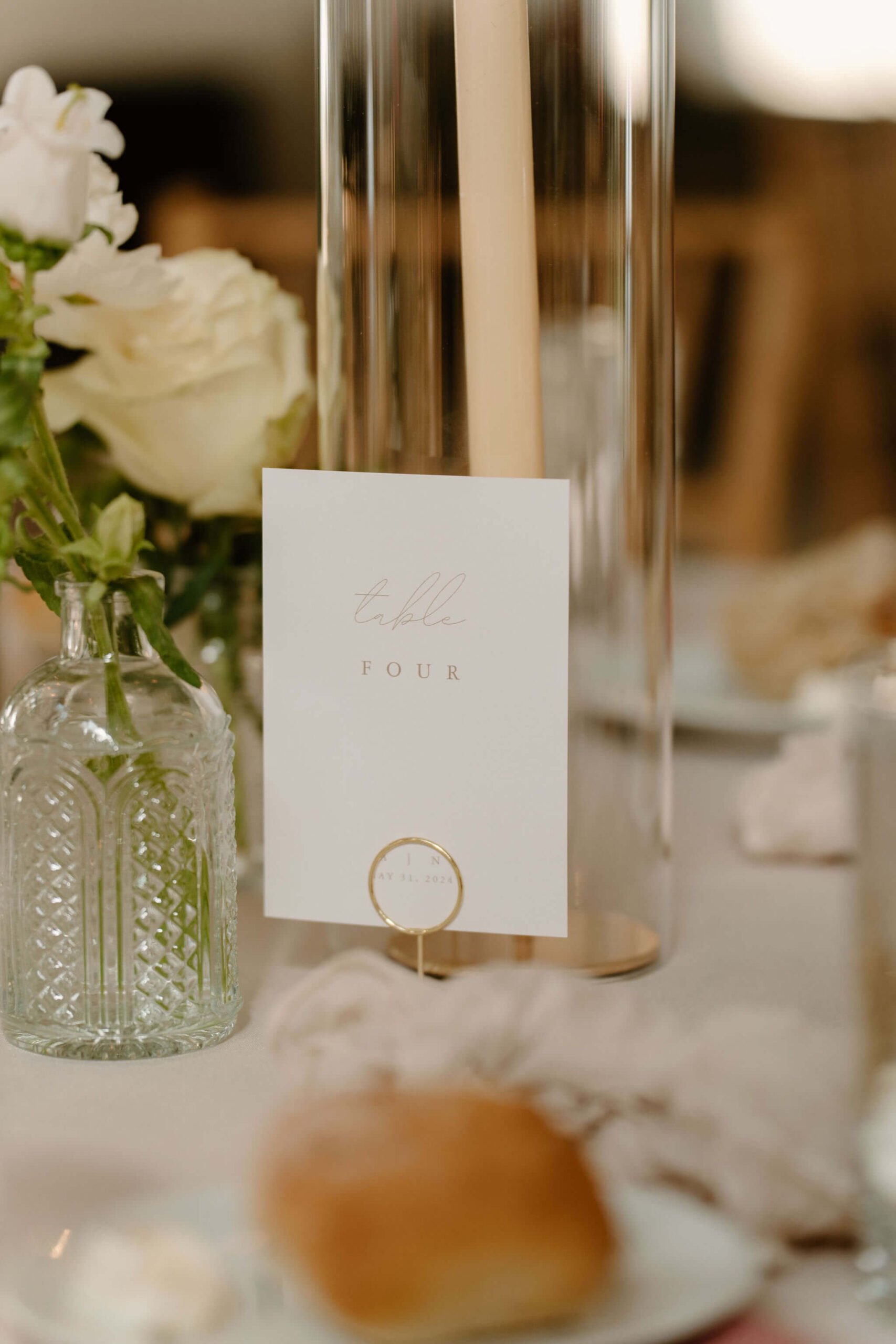 close up of a table number depicting the words "table four", next to a bud vase and candlestick