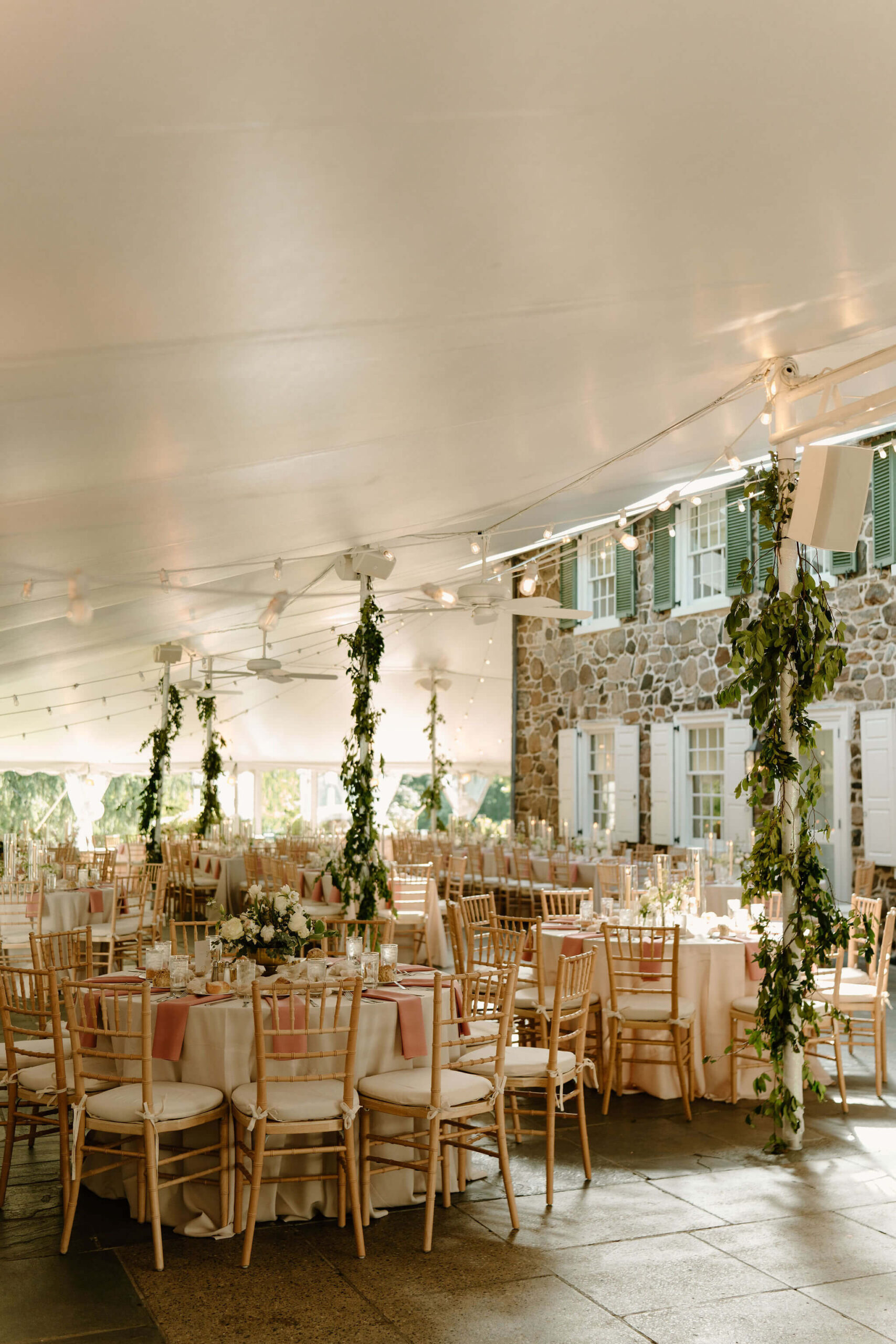 wide image of a reception area, with many tables decorated with greenery, white flowers, and pink napkins