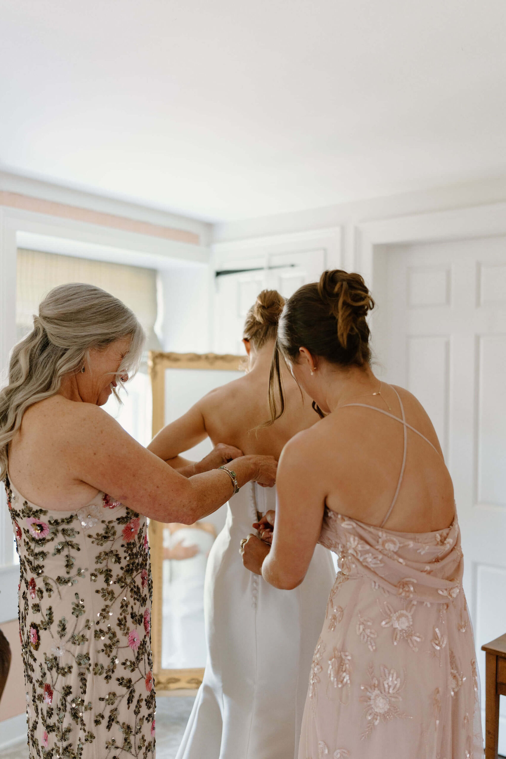 mother of the bride and sister of the bride helping to zip the bride into her wedding dress
