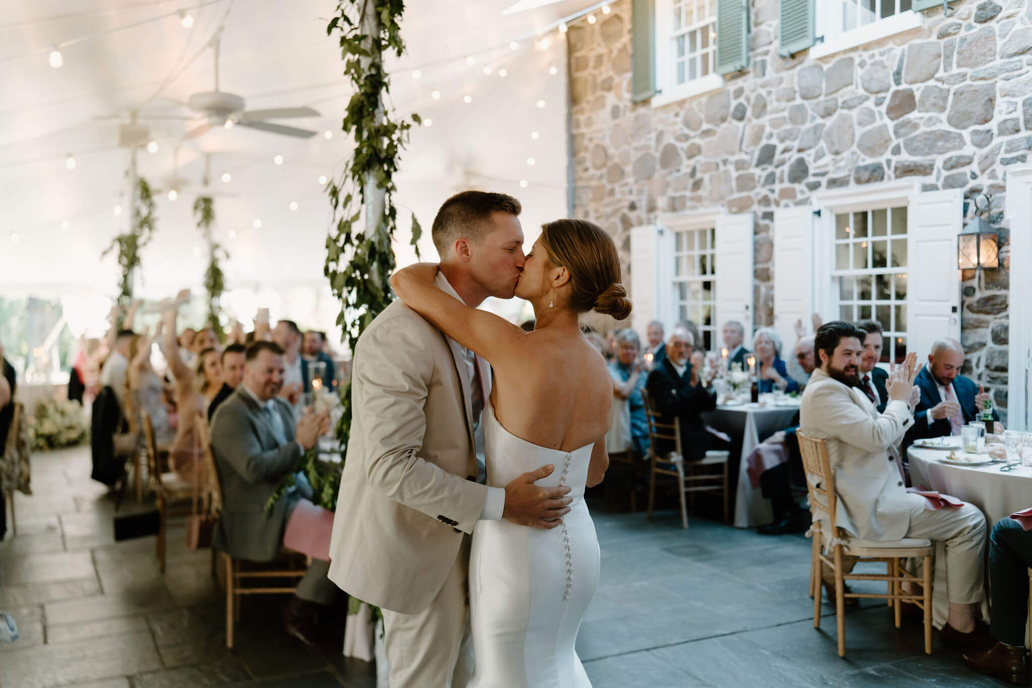 bride and groom kissing during their first dance, guests clapping in the background