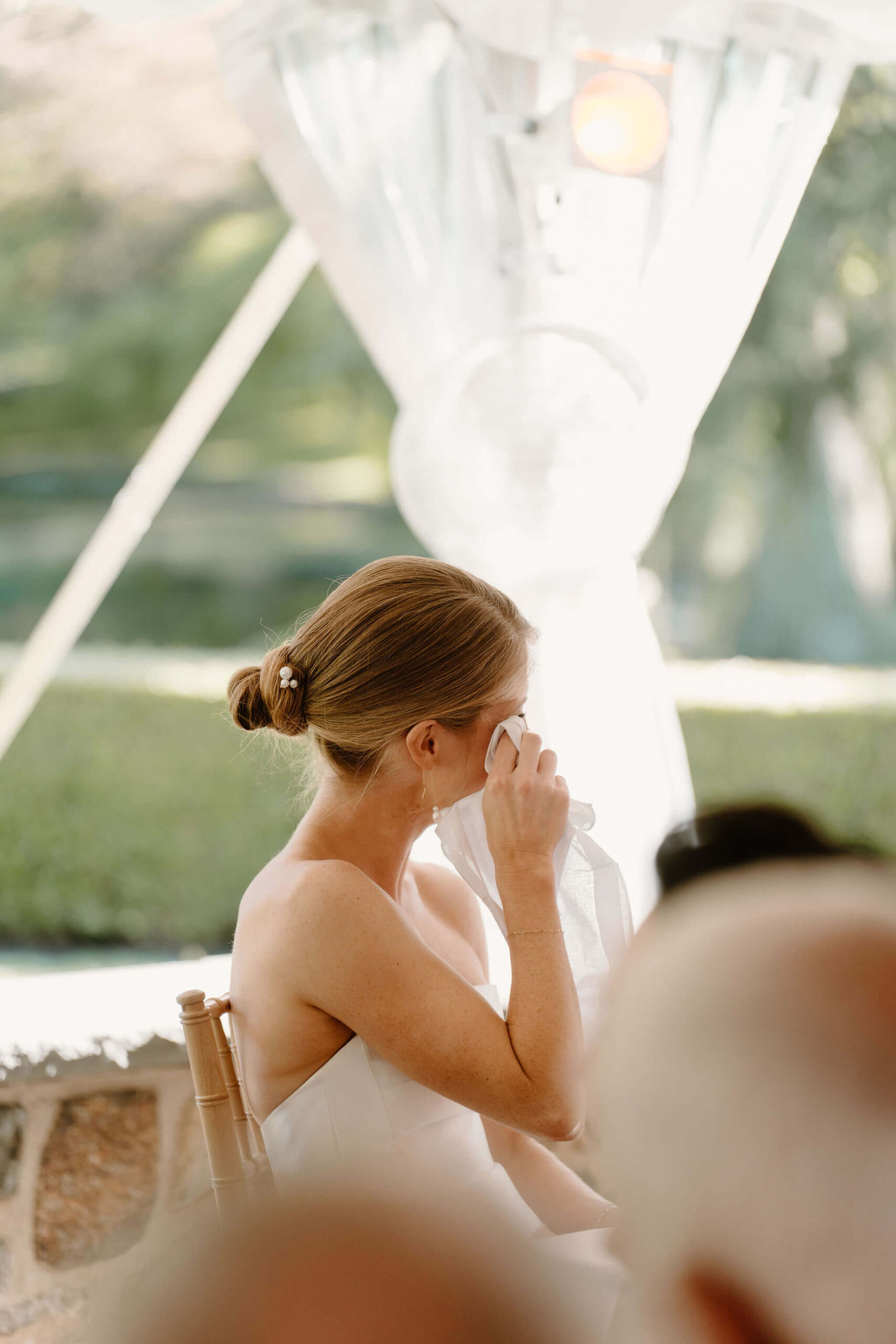 bride seated at sweetheart table, dabbing at her tears with a napkin