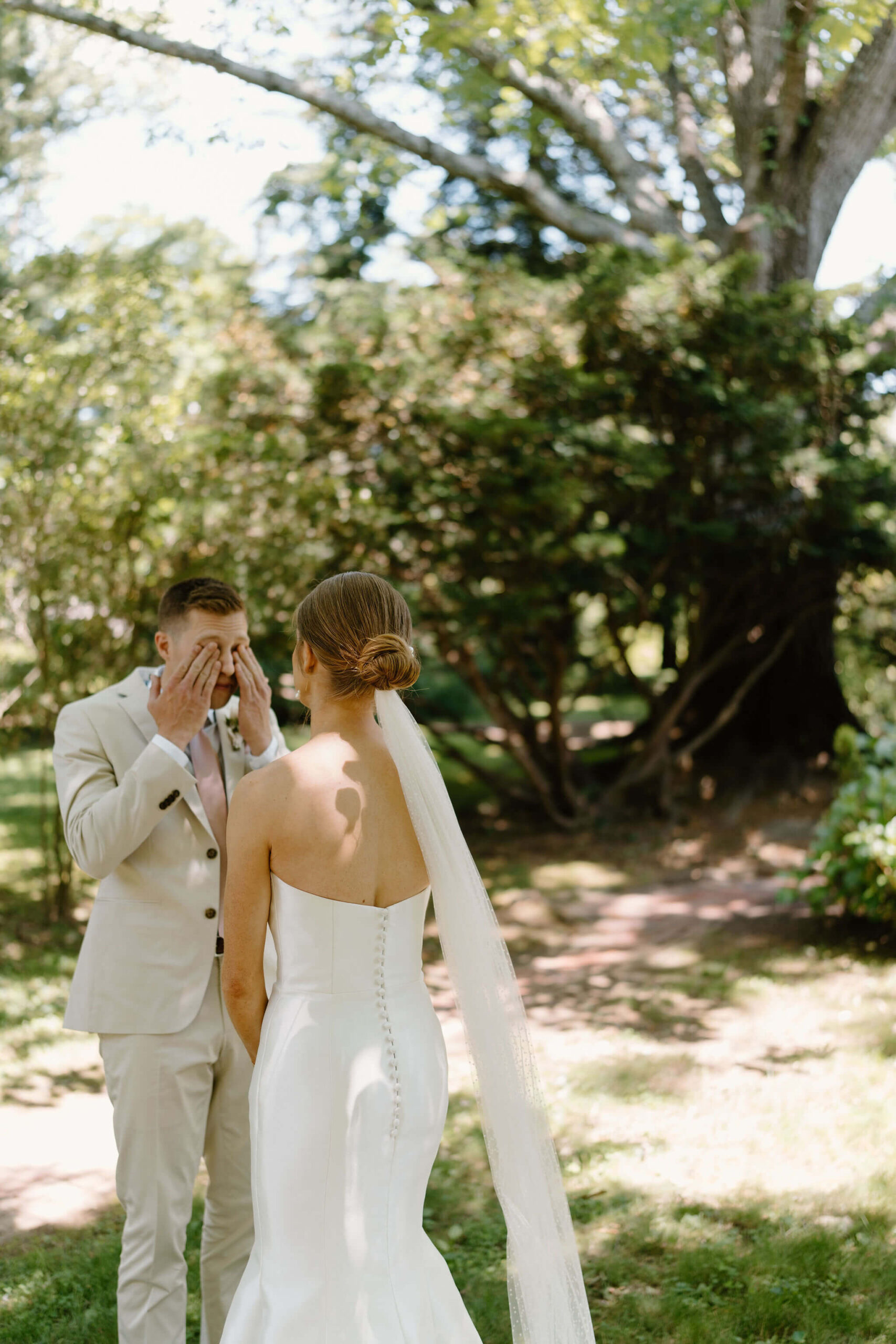 groom (tan suit, pink tie) wiping his eyes with emotion after first look with bride