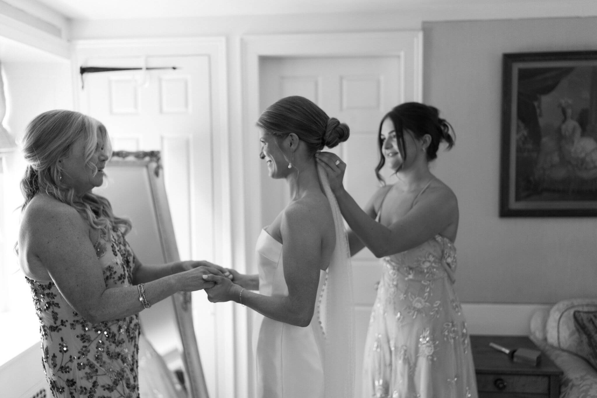 bride holding her mother's hands (off camera), while the sister of the bride fixes the bride's veil underneath her bun
