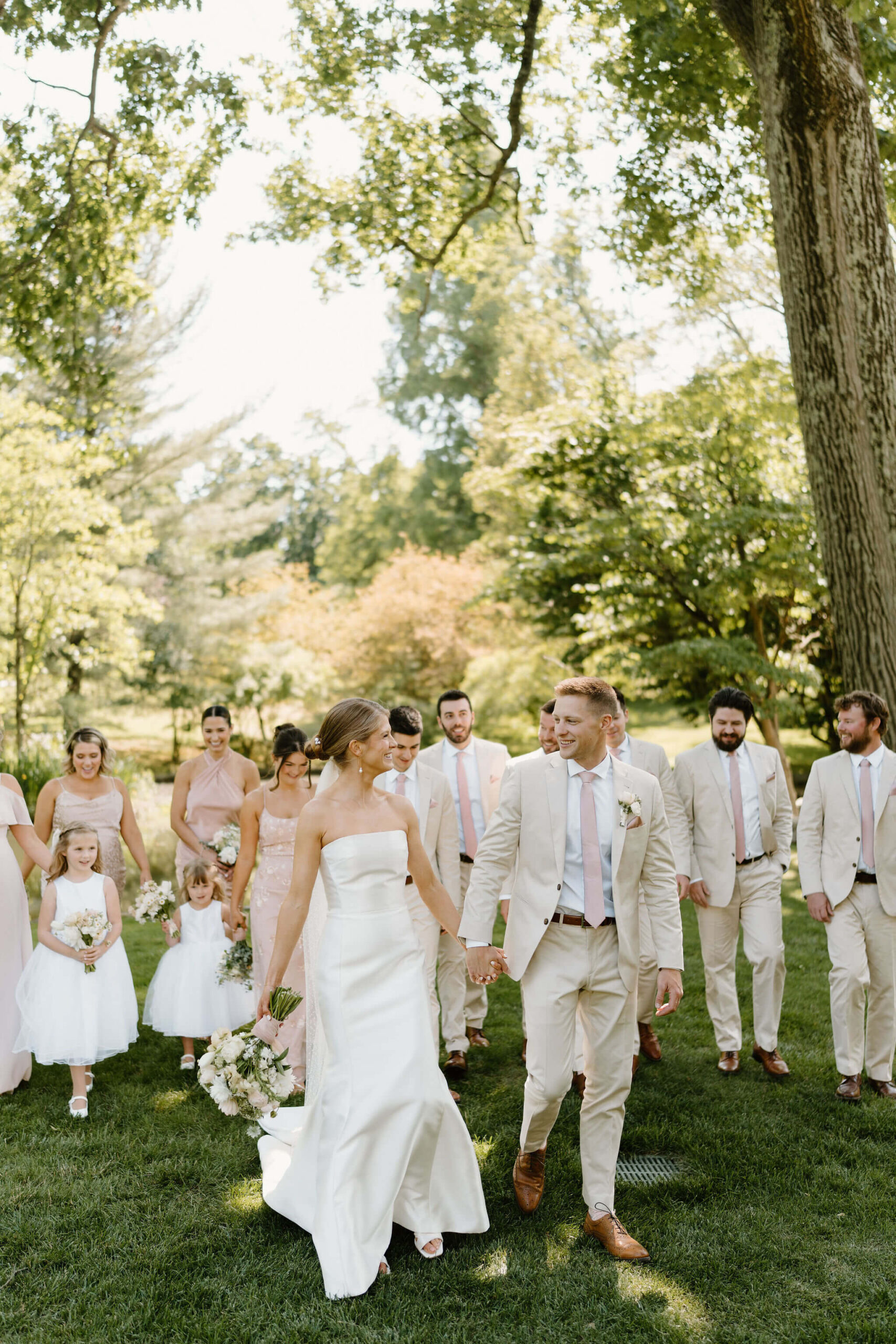 wedding party all smiling and walking toward the camera together, bride and groom in front of them on a beautiful spring day