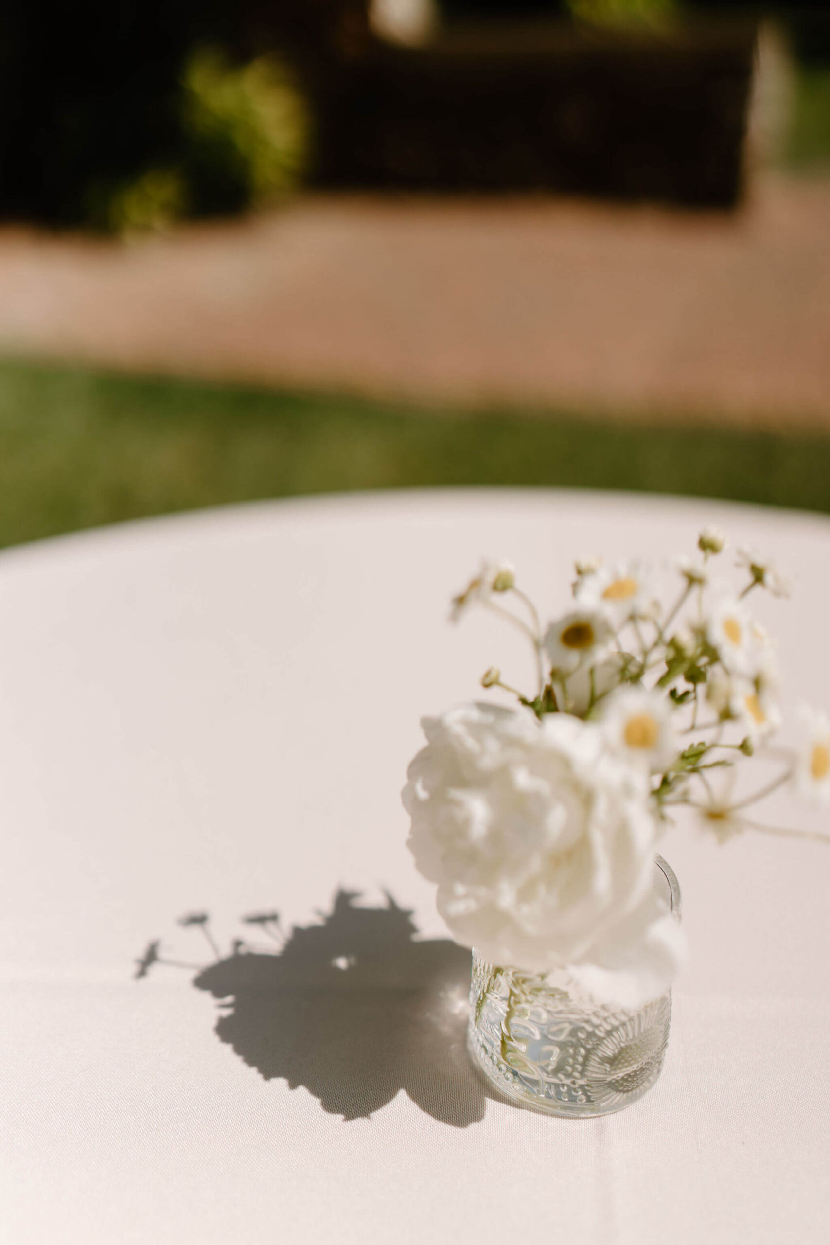 close up image of a small centerpiece of a white flowers, casting a harsh shadow on a white tablecloth