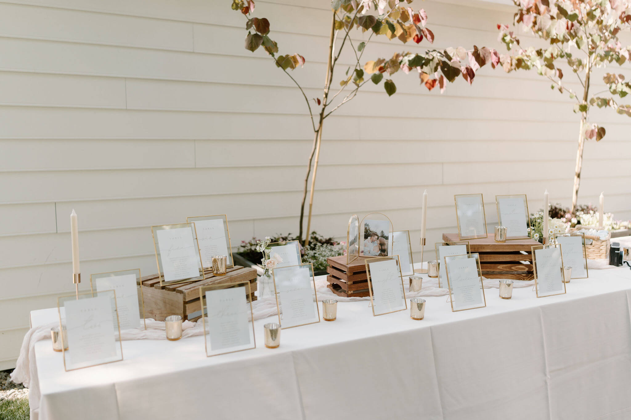 table seating charts on white paper, framed in gold, set up on a white tablecloth with gold candle votives 