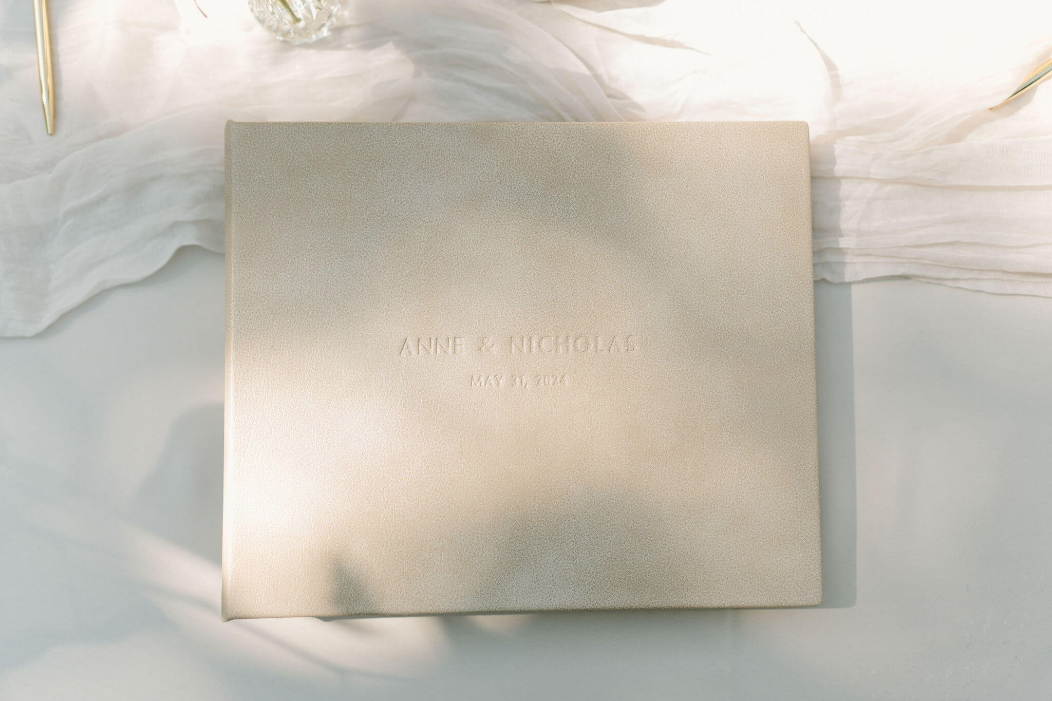 white leather guest book with "anne & nicholas" written on it, arranged on a table with shadows across the book