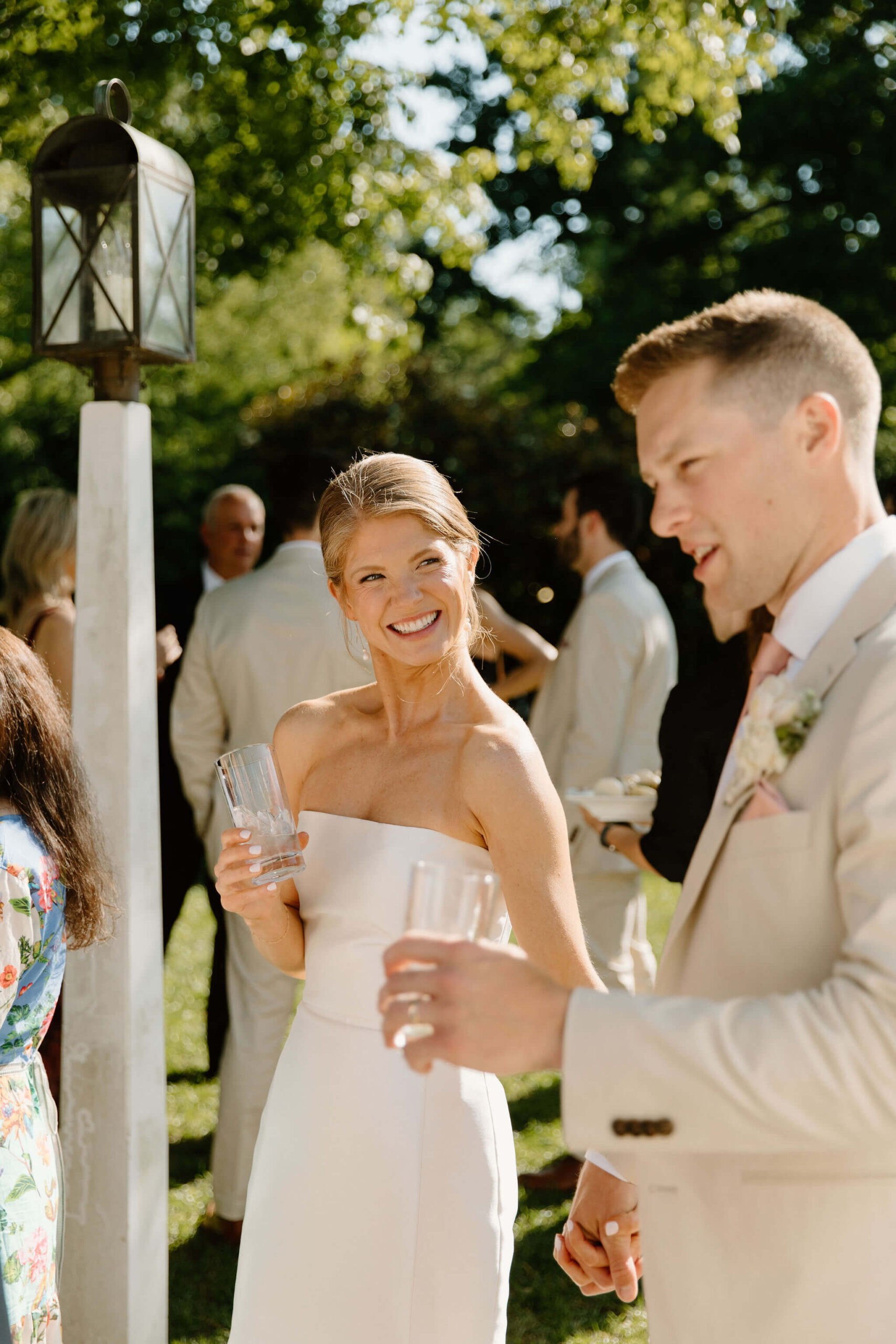 bride smiling at her groom as he talks to guests at cocktail hour