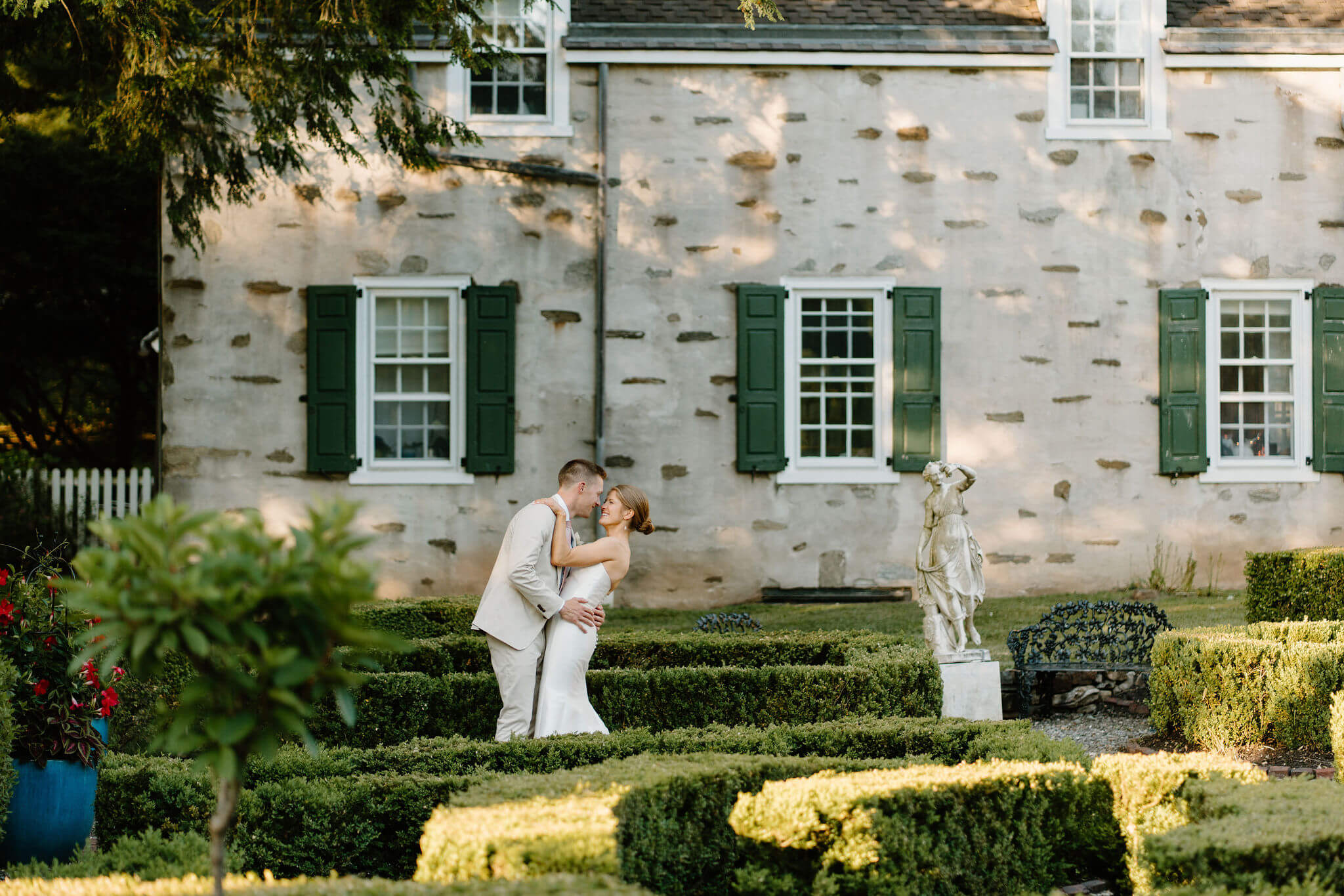 bride and groom embracing in a hedge maze, with an old stone home behind them