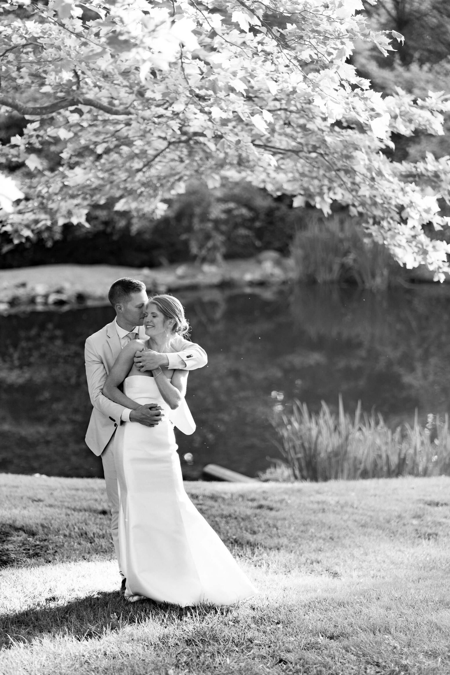 black and white image of bride and groom with arms wrapped around each other, groom kissing her on the temple