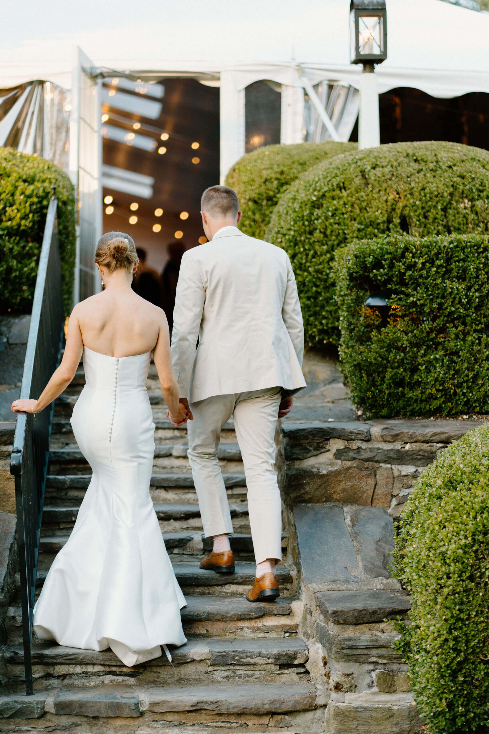 groom and bride walking up stone steps to the tent housing their wedding reception
