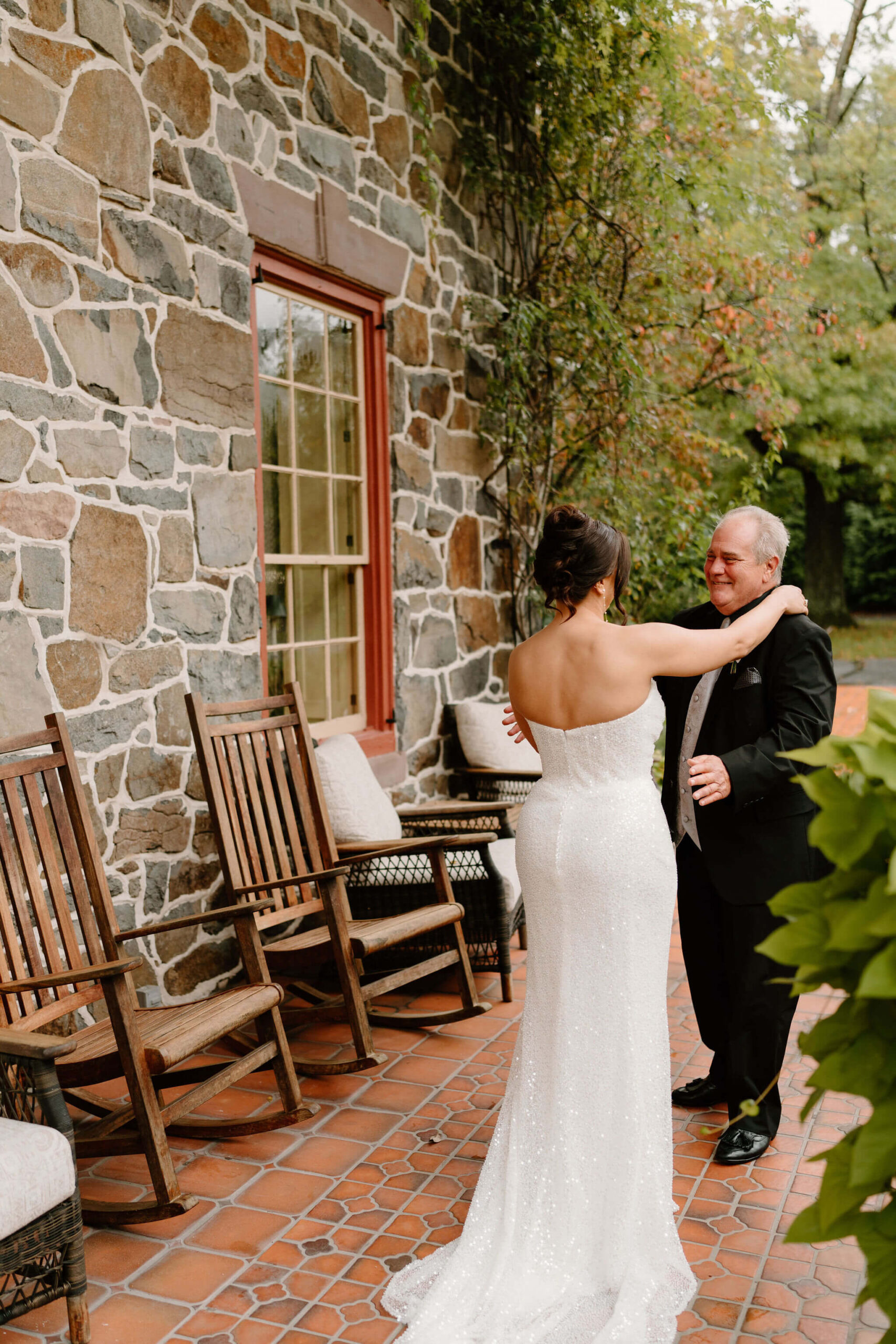 bride hugging her father after their first look on her wedding day, against a stone home background