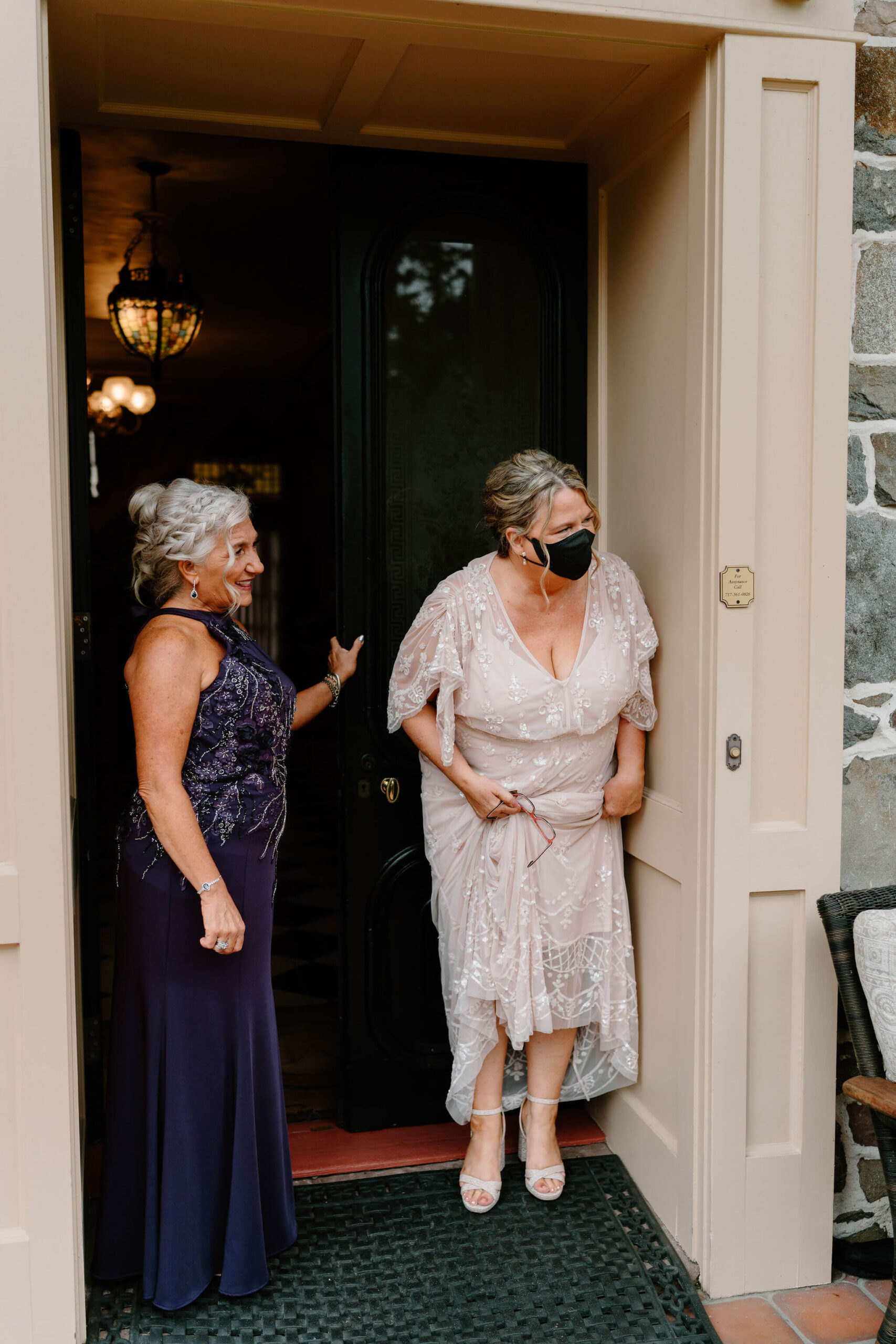 mother of the bride and mother of the groom peeking around a doorframe to watch the first look