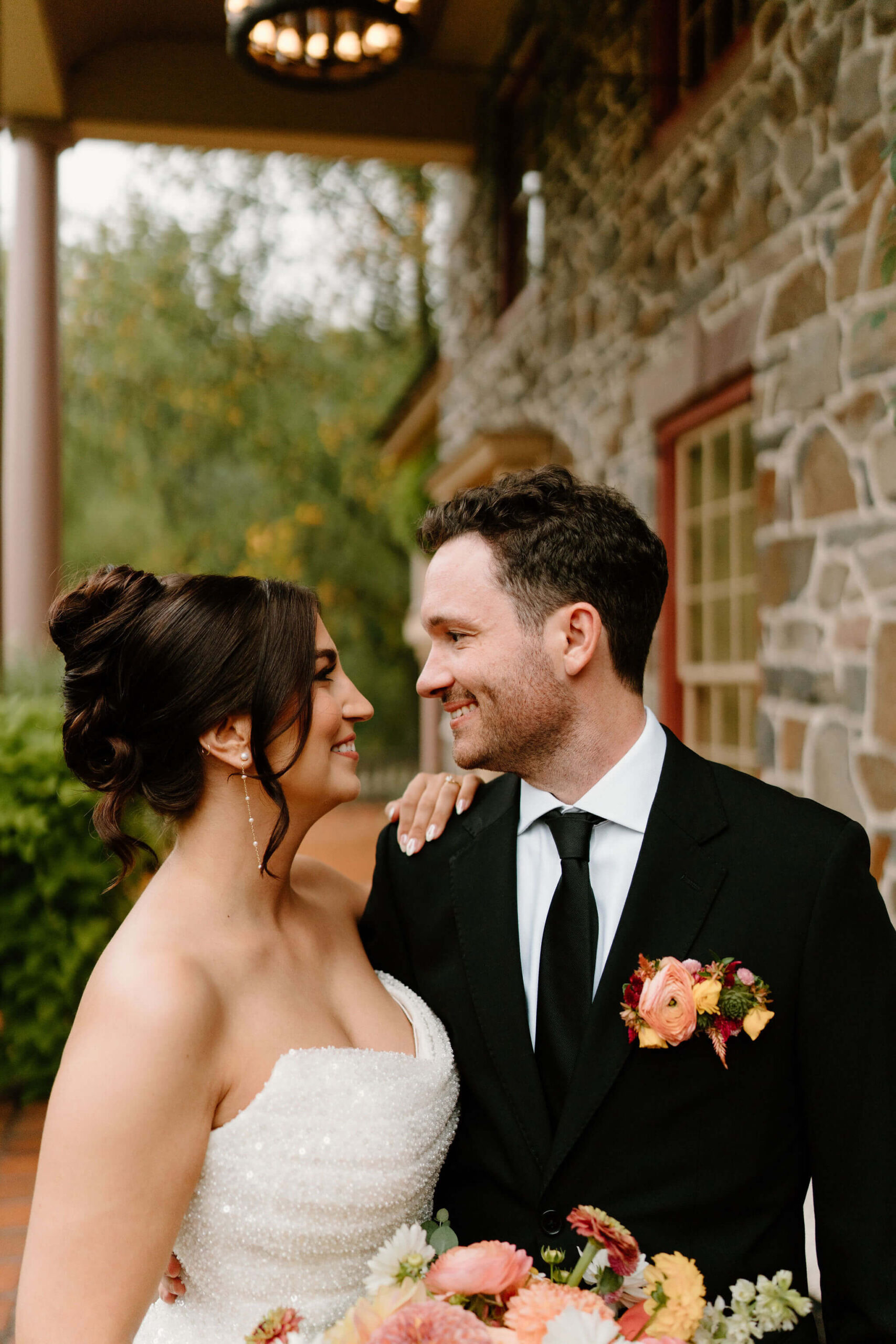 bride and groom on covered stone porch, smiling at each other on their rainy wedding day