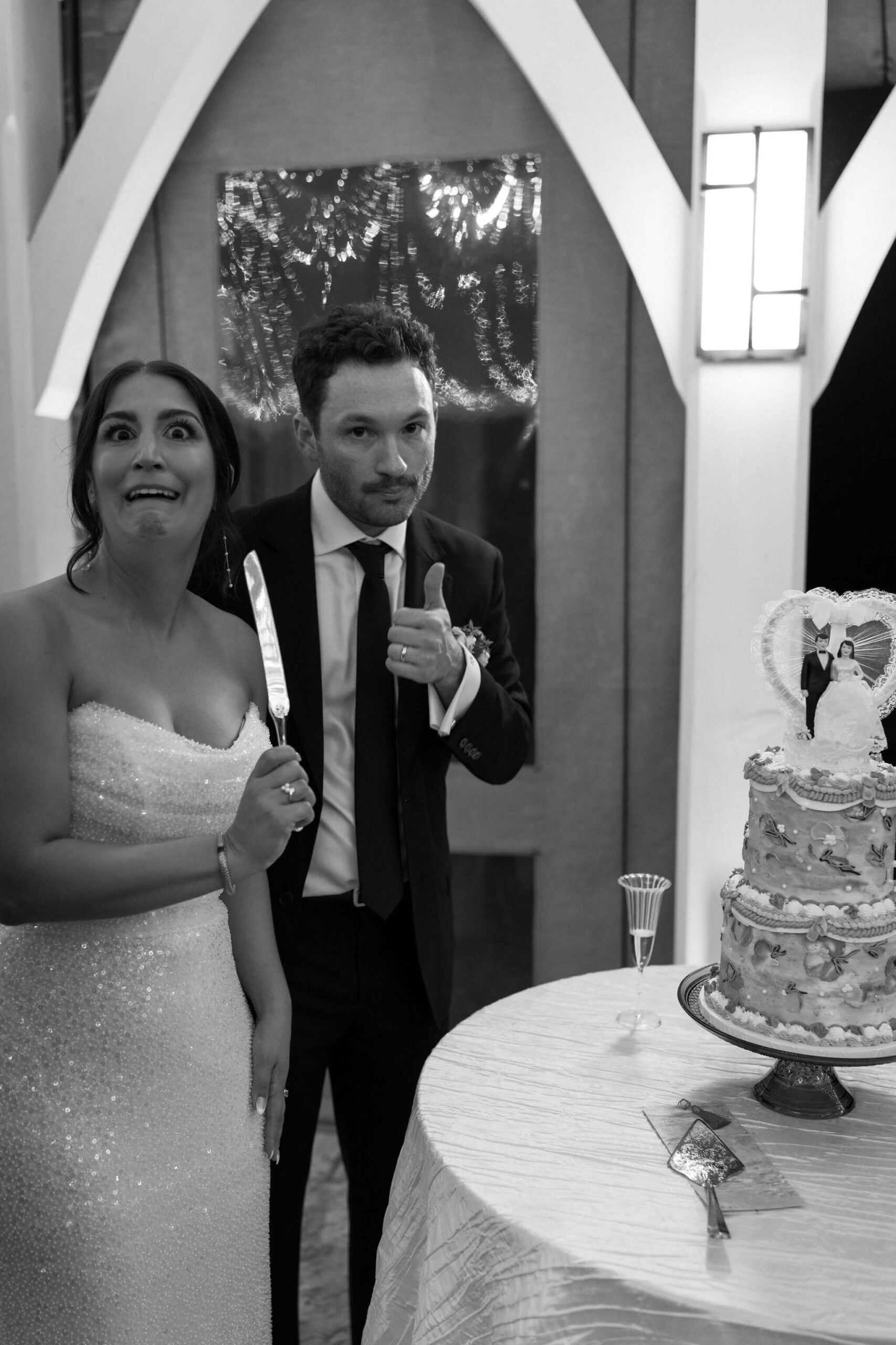 black and white image of bride and groom making silly faces as they prepare to cut their wedding cake