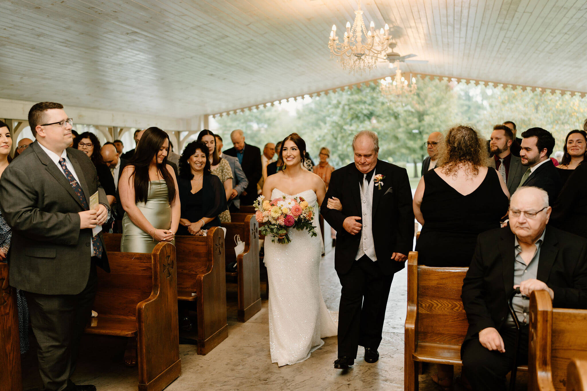 bride smiling as her father walks her down the aisle during her wedding ceremony beneath a large pavilion