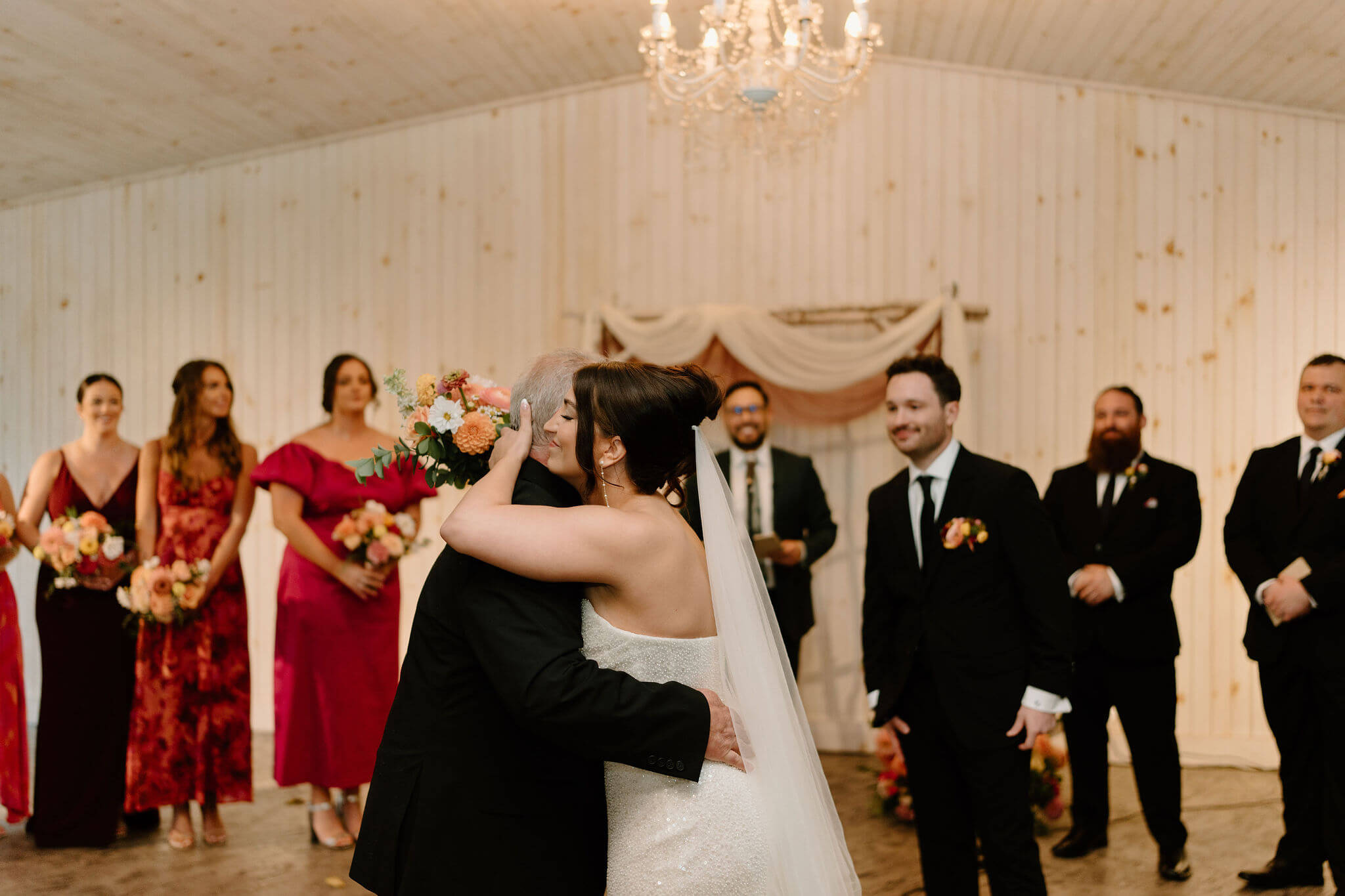 bride and father embracing at the start of her wedding ceremony, groom approaching in the background
