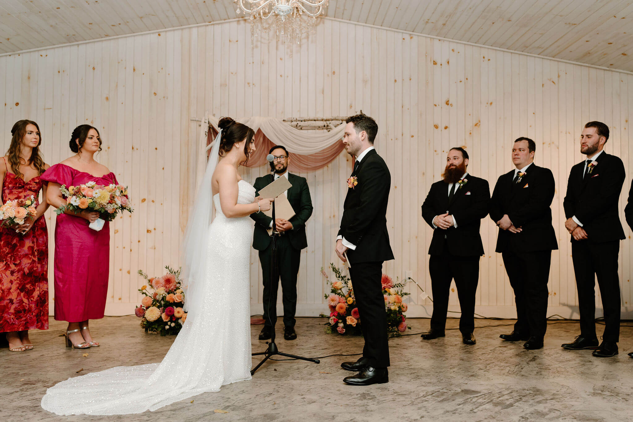 bride exchanging her vows to her groom, bridal party and officiant watching behind them