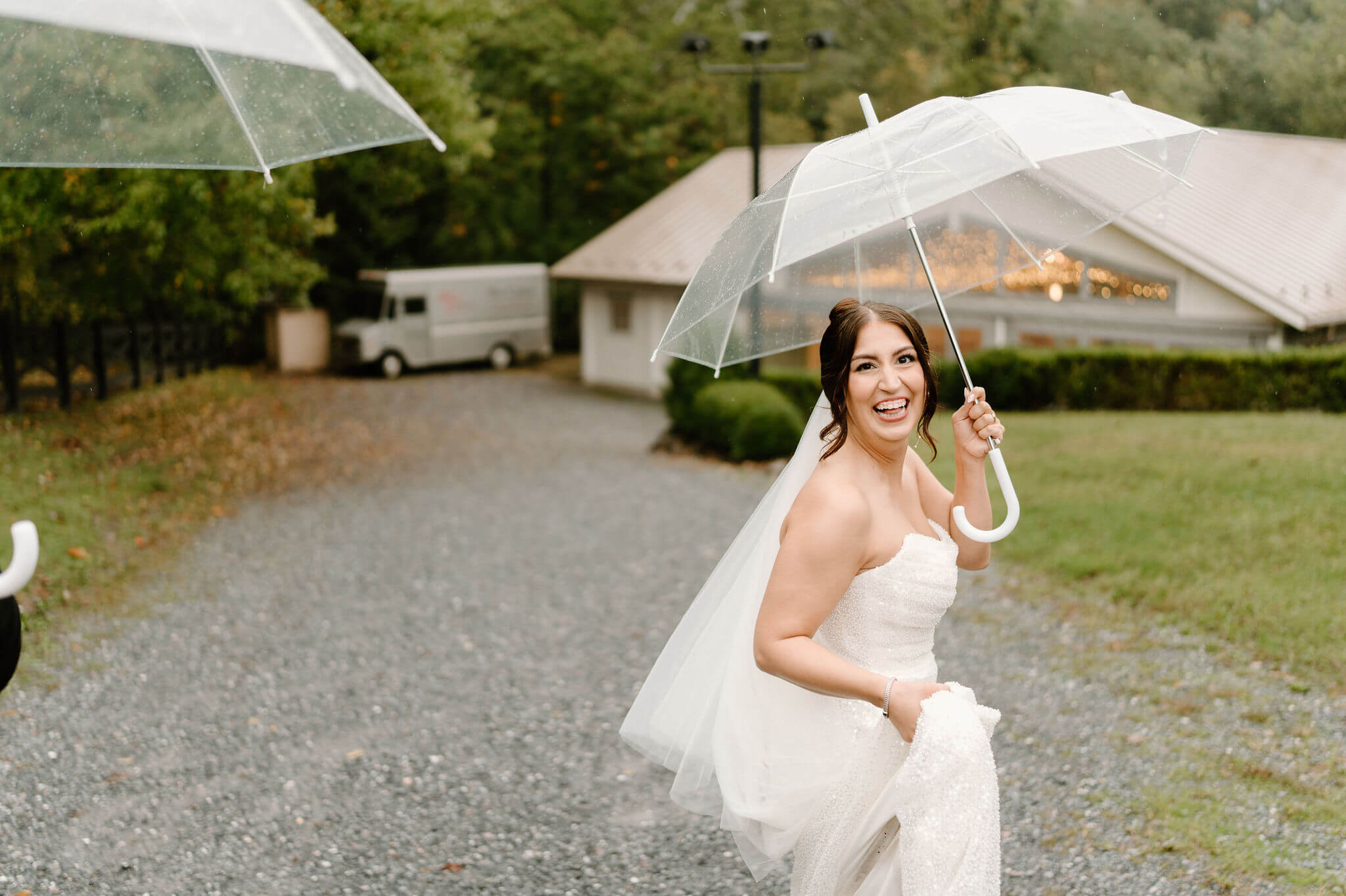 bride smiling widely after wedding ceremony, holding clear umbrella under rainy skies