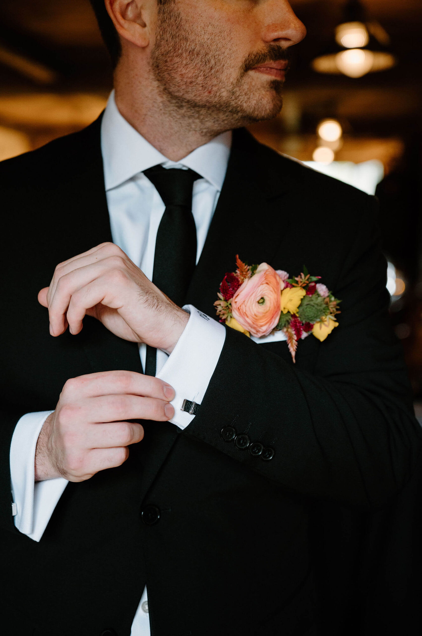 close up image of groom's cuff links and colorful boutonniere against his black suit as he looks off camera