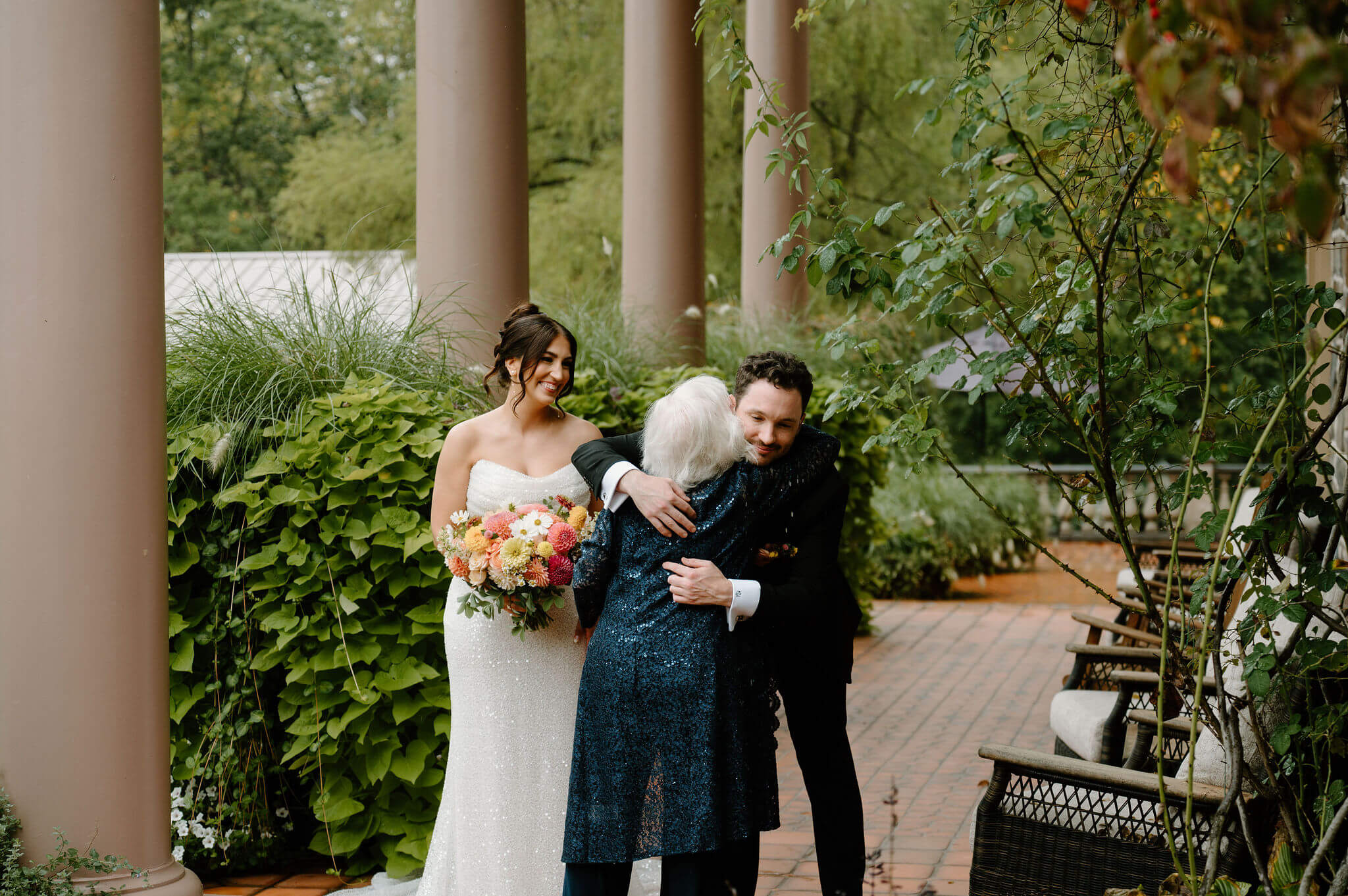groom hugging grandmother as she arrives to their wedding, bride smiling in the background
