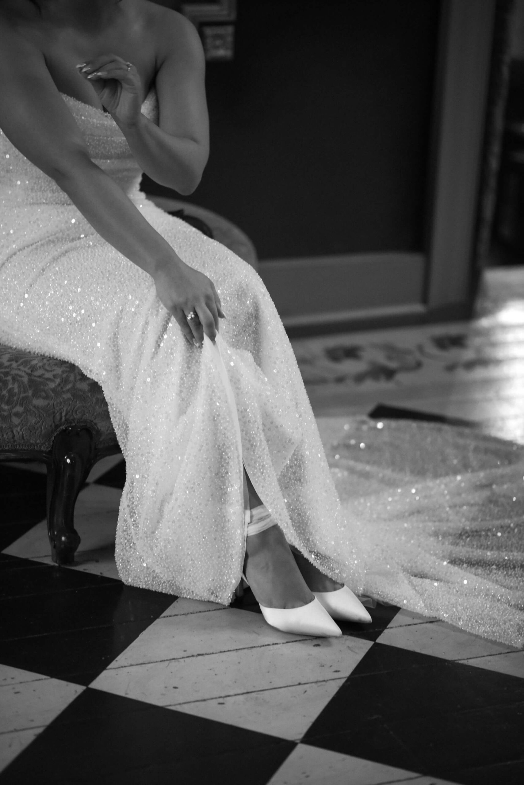 close up of bride's white shoes beneath the skirt of her sequined wedding dress, bride seated on a chair