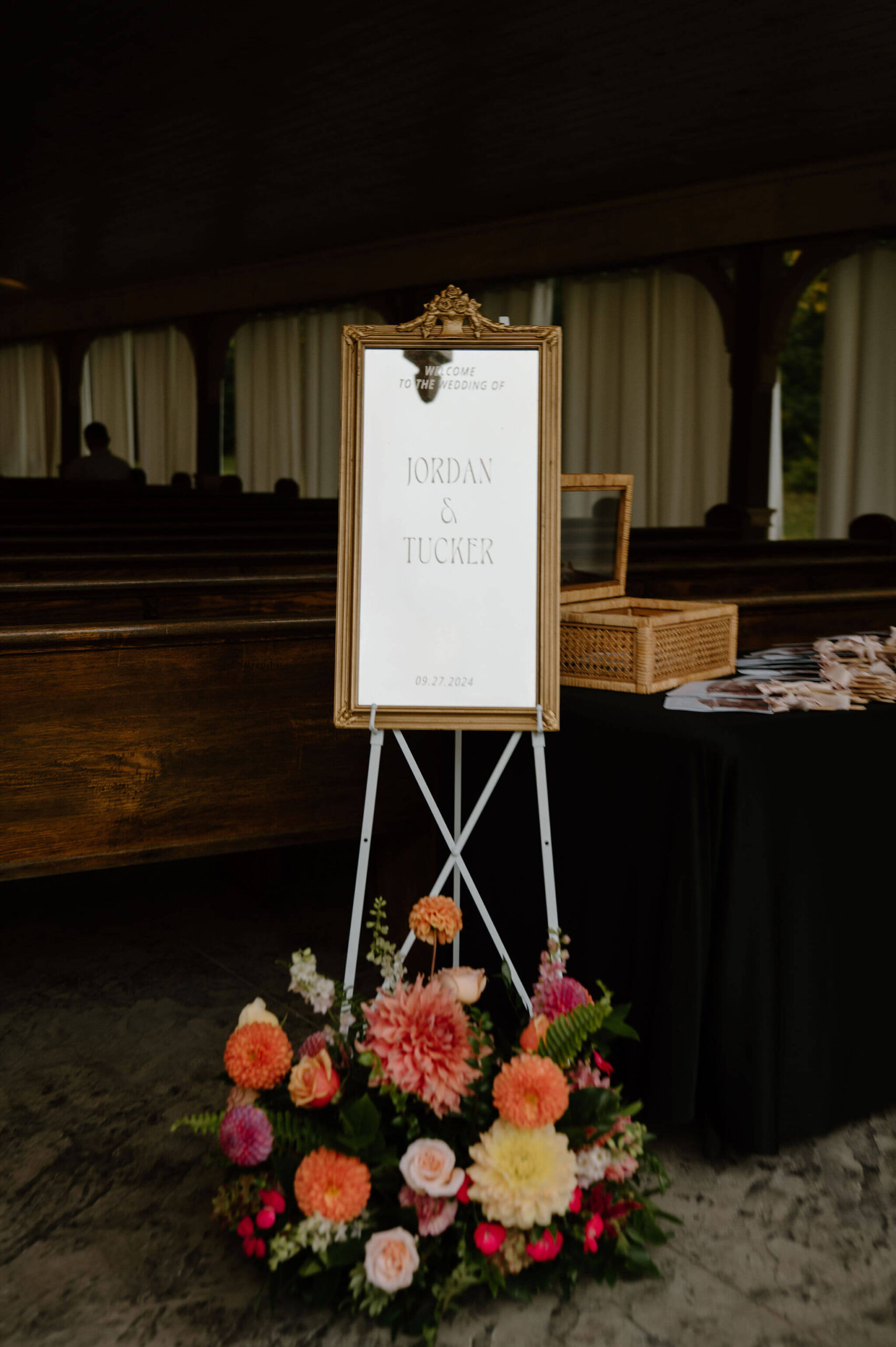 gold-rimmed mirror with a decal reading "Jordan & Tucker" set up at the ceremony site, a large colorful floral piece at the bottom of the easle