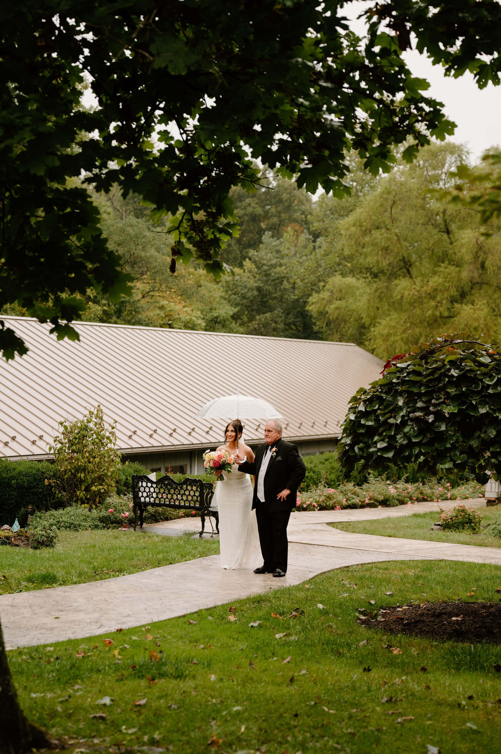 bride and her father waiting to enter the wedding ceremony together, beneath a clear umbrella