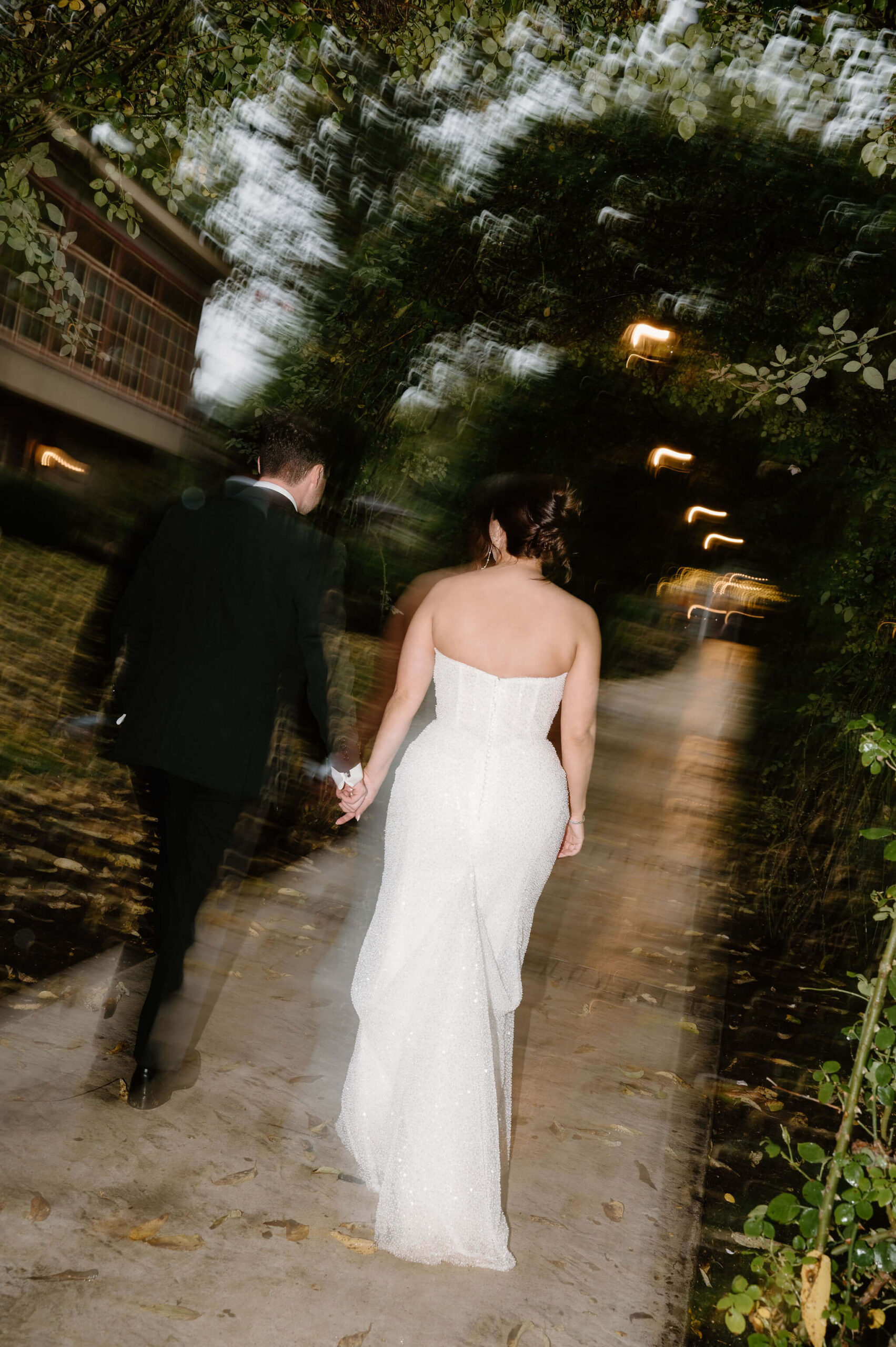 shutter drag image with flash of bride and groom walking back up a garden pathway toward their wedding reception