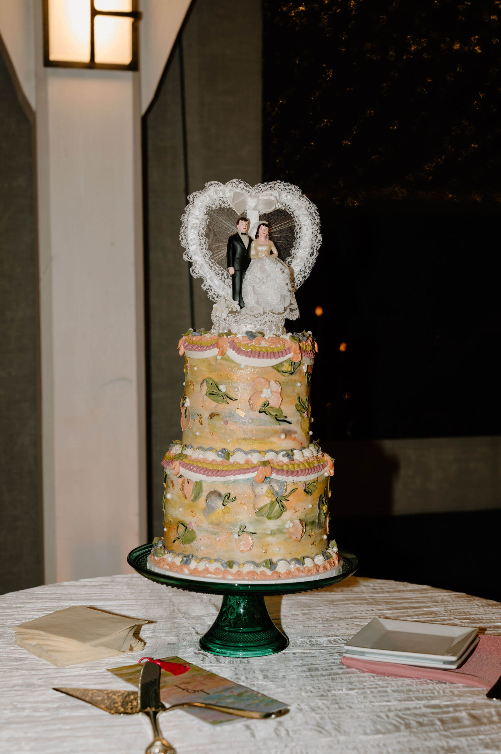 a colorful vintage-style wedding cake, decorated with pink, orange, and green trip, a watercolor design, and topped with a vintage cake topper