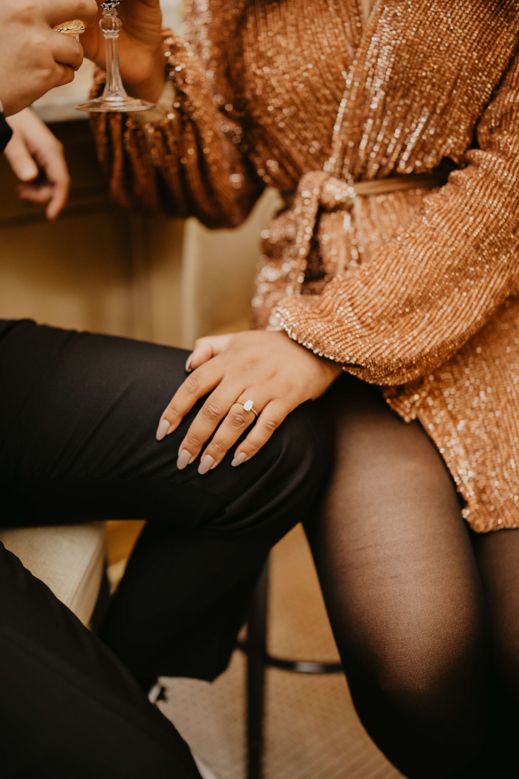 close up of engagement ring on bride's hand, with her hand on groom's knee